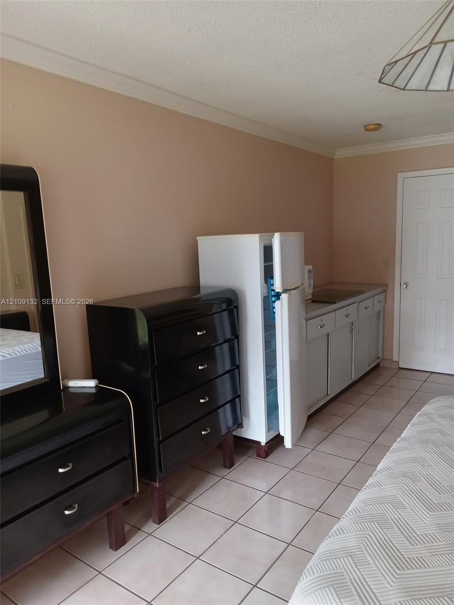 Kitchenette area featuring light-toned cabinetry, a compact refrigerator, a recessed sink, and tile flooring