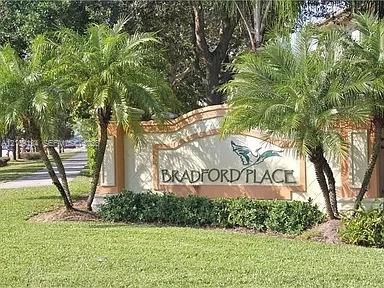Stucco masonry monument sign featuring dimensional lettering, decorative trim, and mature landscaping including palm trees