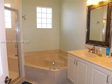 Bathroom featuring a corner soaking tub, glass-enclosed shower, vanity with a stone countertop, and block-style privacy window