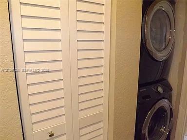 Laundry area featuring white bi-fold louvered doors and a stacked front-load washer and dryer unit