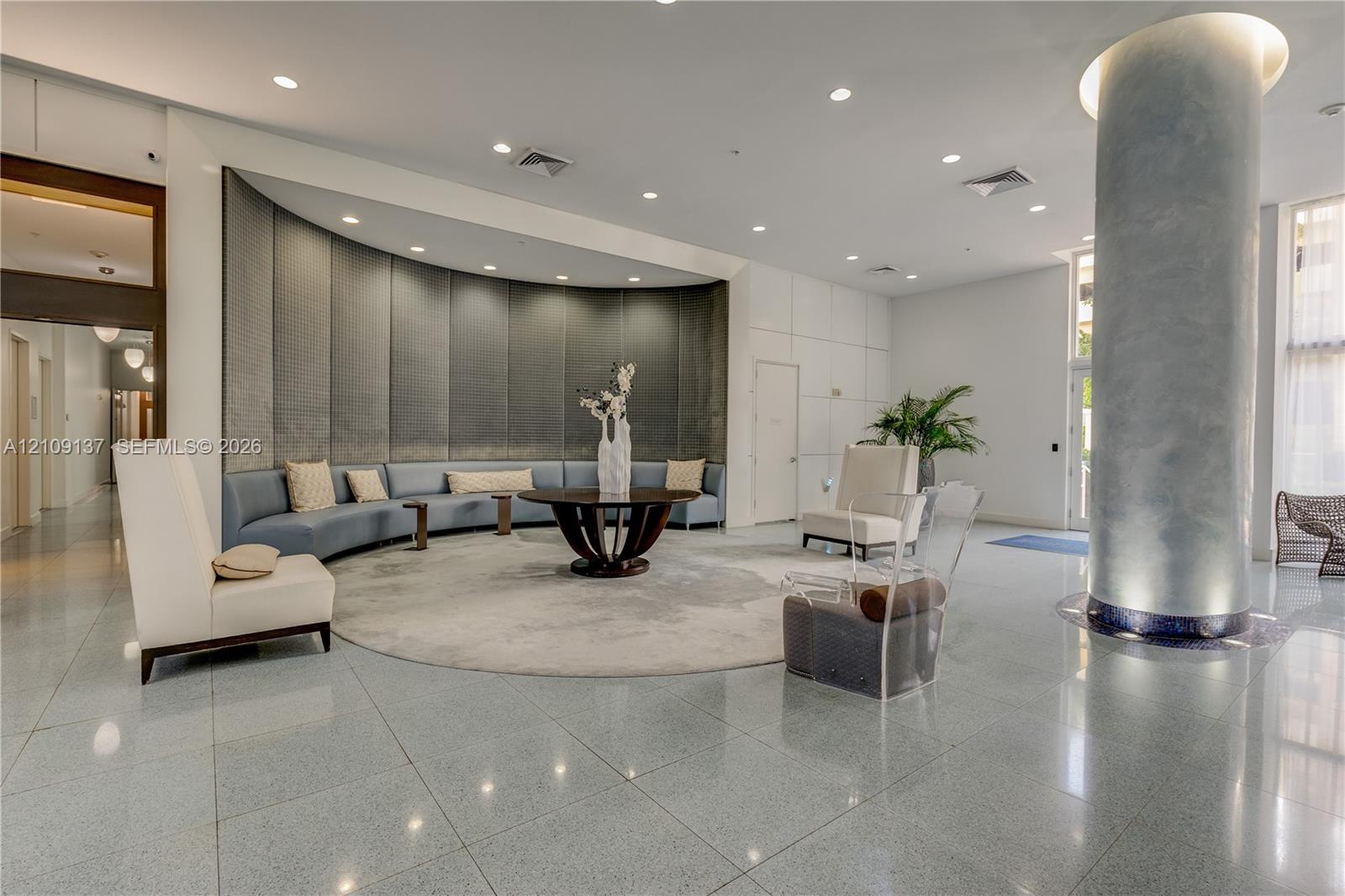 Lobby featuring polished stone flooring, a prominent structural column with metallic-finish cladding, recessed lighting, and a curved, paneled feature wall