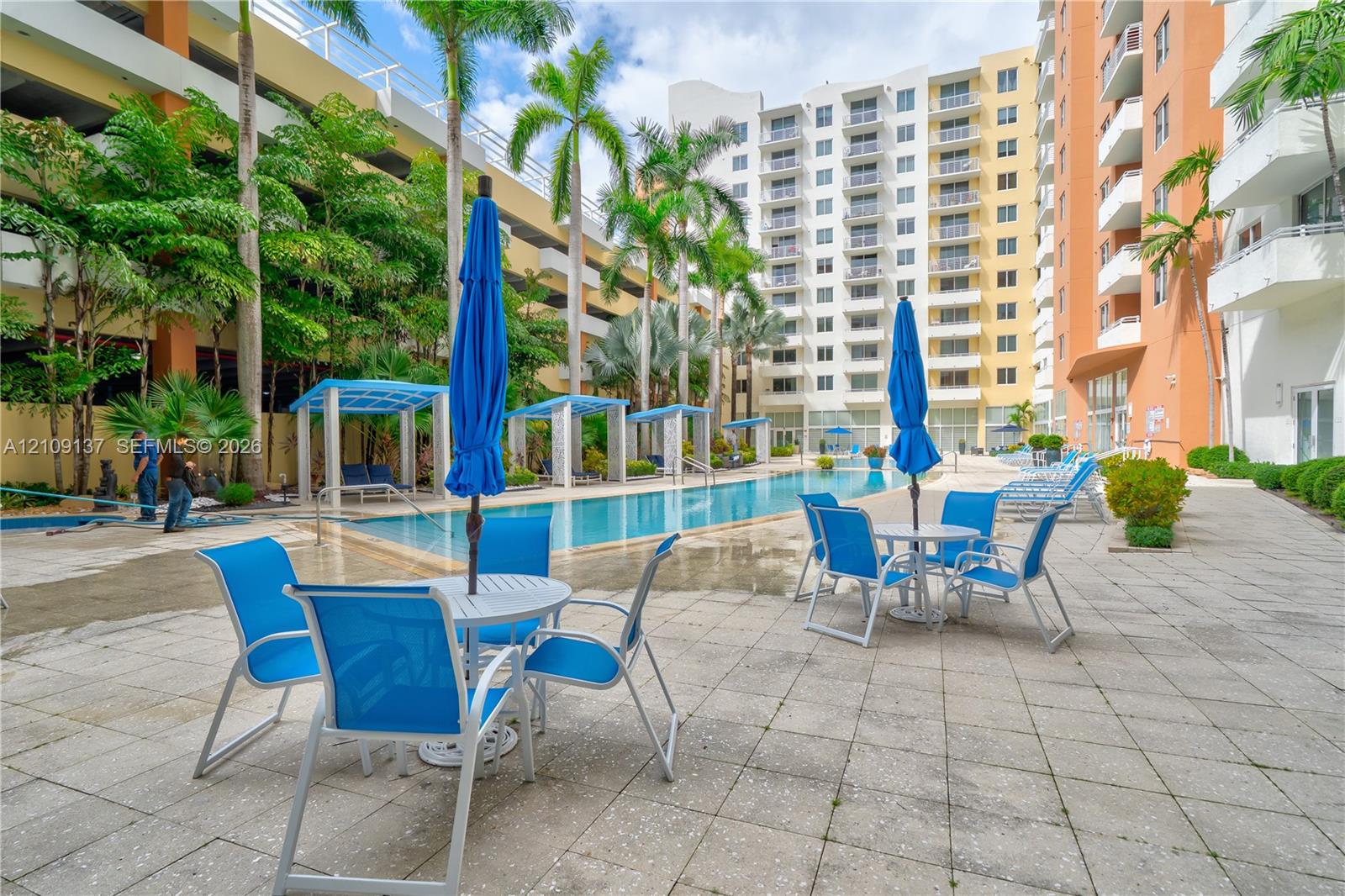 Outdoor recreation area featuring a swimming pool, tiled sundeck, multiple cabanas, and mature palm trees