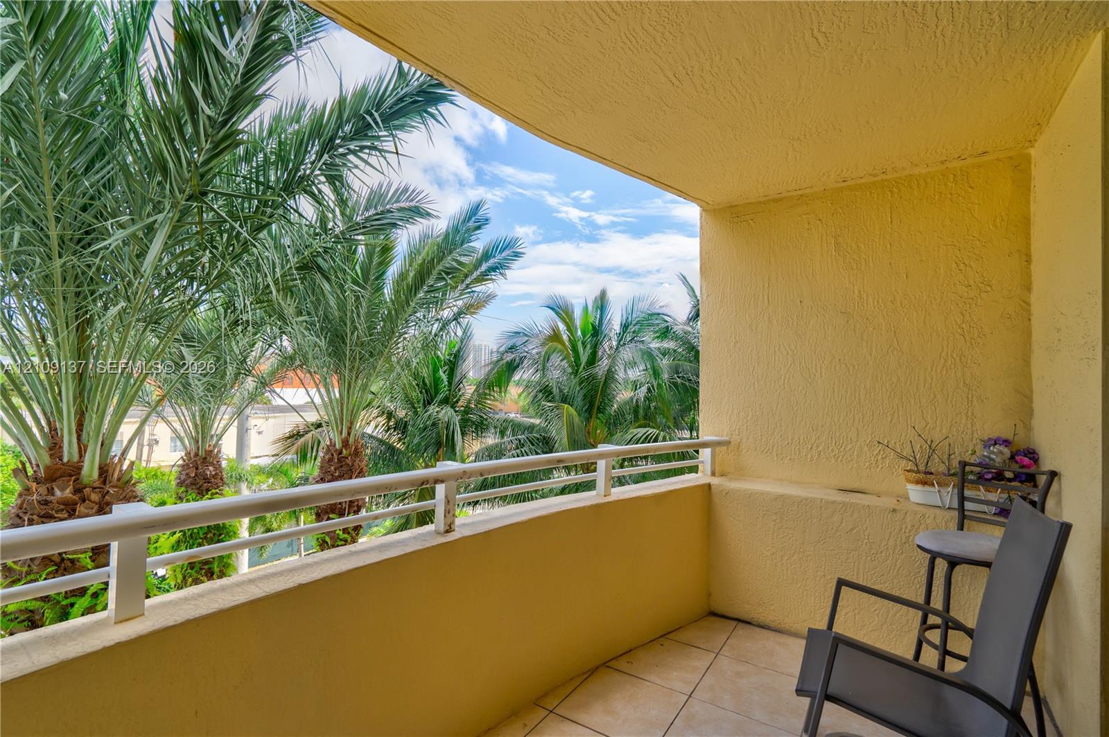 Covered balcony with textured stucco walls, tiled flooring, and a metal railing