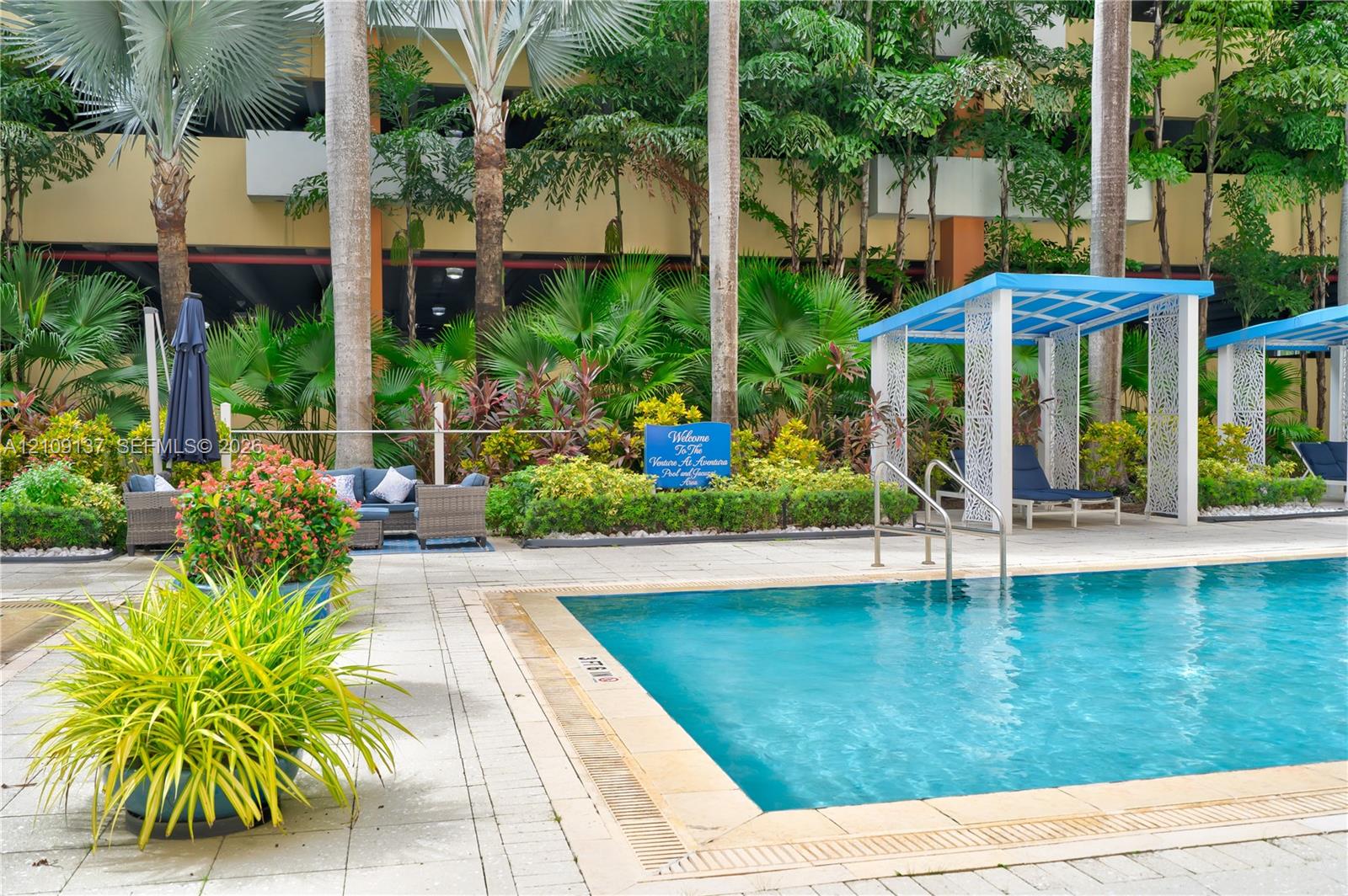 Swimming pool with masonry coping, paver patio, and integrated shade structures surrounded by lush tropical landscaping