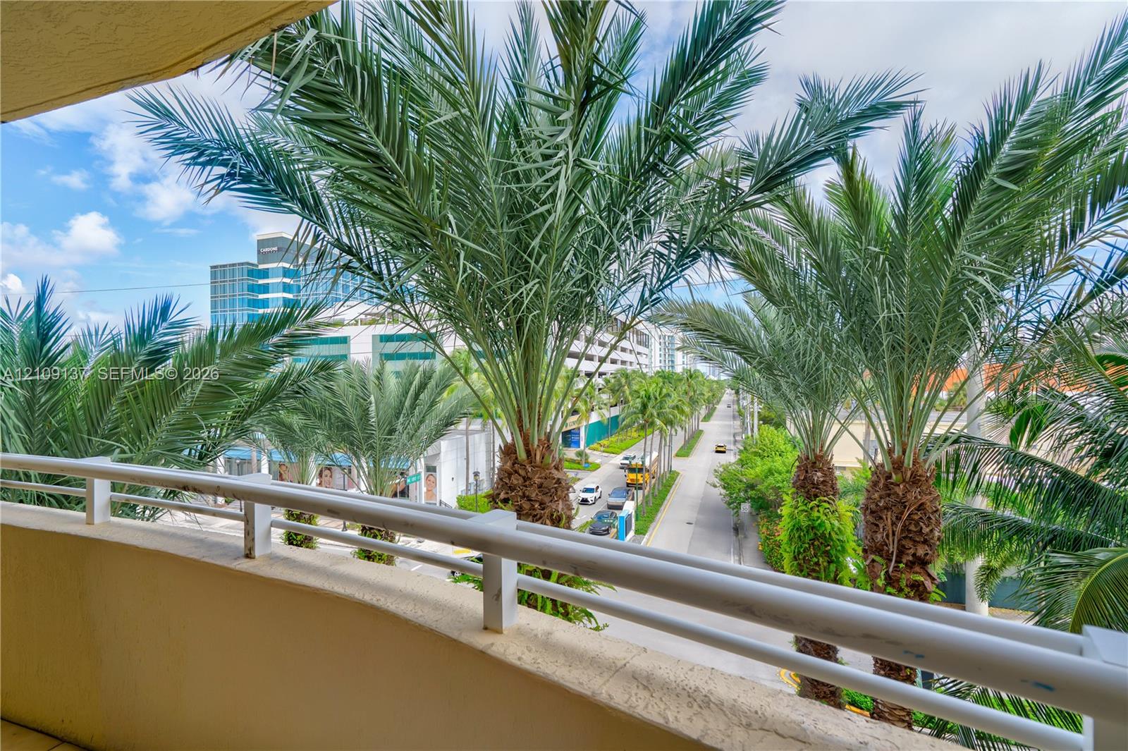 Covered balcony with white metal railings and mature palm trees