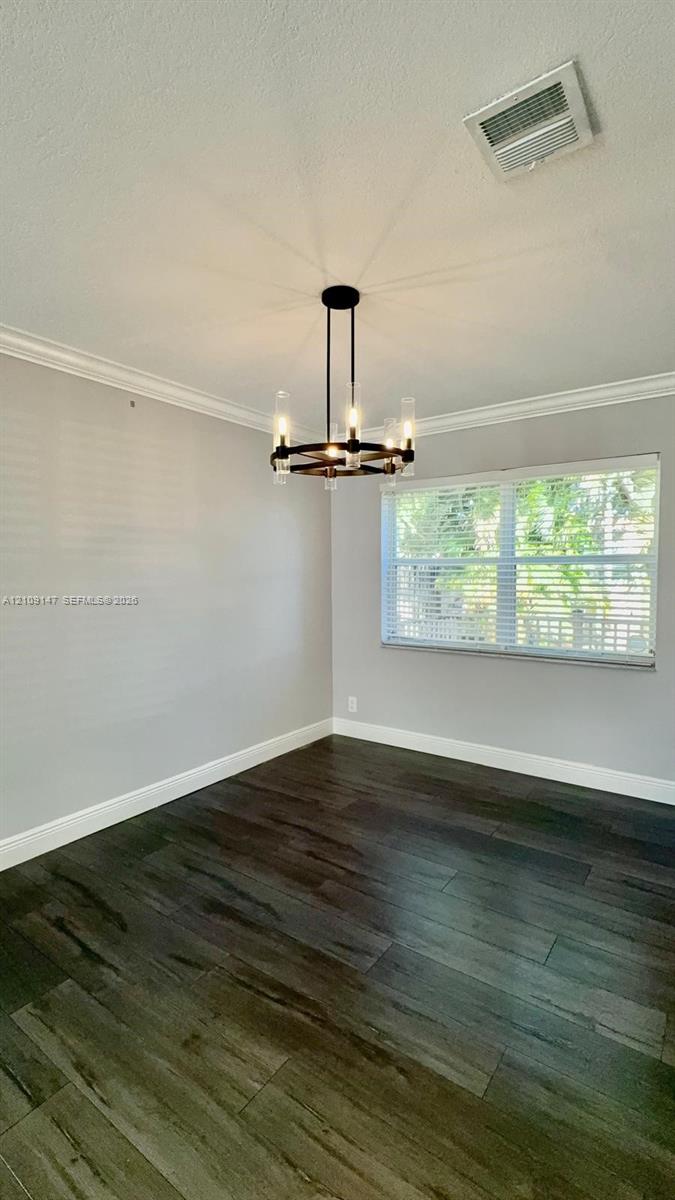 Interior space featuring wood-finish flooring, crown molding, and a multi-light chandelier with glass cylinders Interior space featuring wood-finish flooring, crown molding, and a multi-light chandelier with glass cylinders