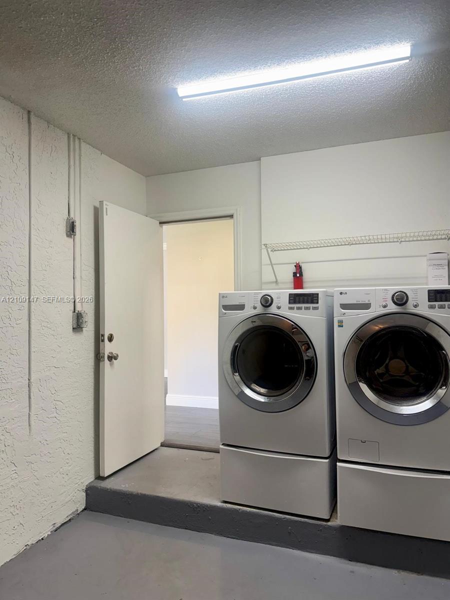 Laundry area featuring white front-load washer and dryer on pedestals, overhead wire shelving, textured wall finish, and painted concrete flooring