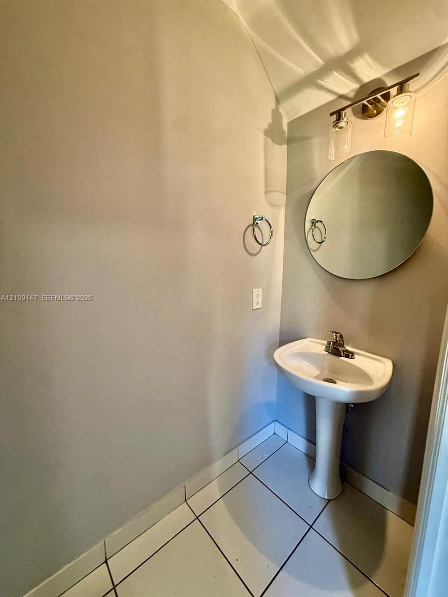 Pedestal sink with a center-set faucet, round frameless mirror, and three-light vanity fixture featuring cylindrical glass shades Pedestal sink with a center-set faucet, round frameless mirror, and three-light vanity fixture featuring cylindrical glass shades