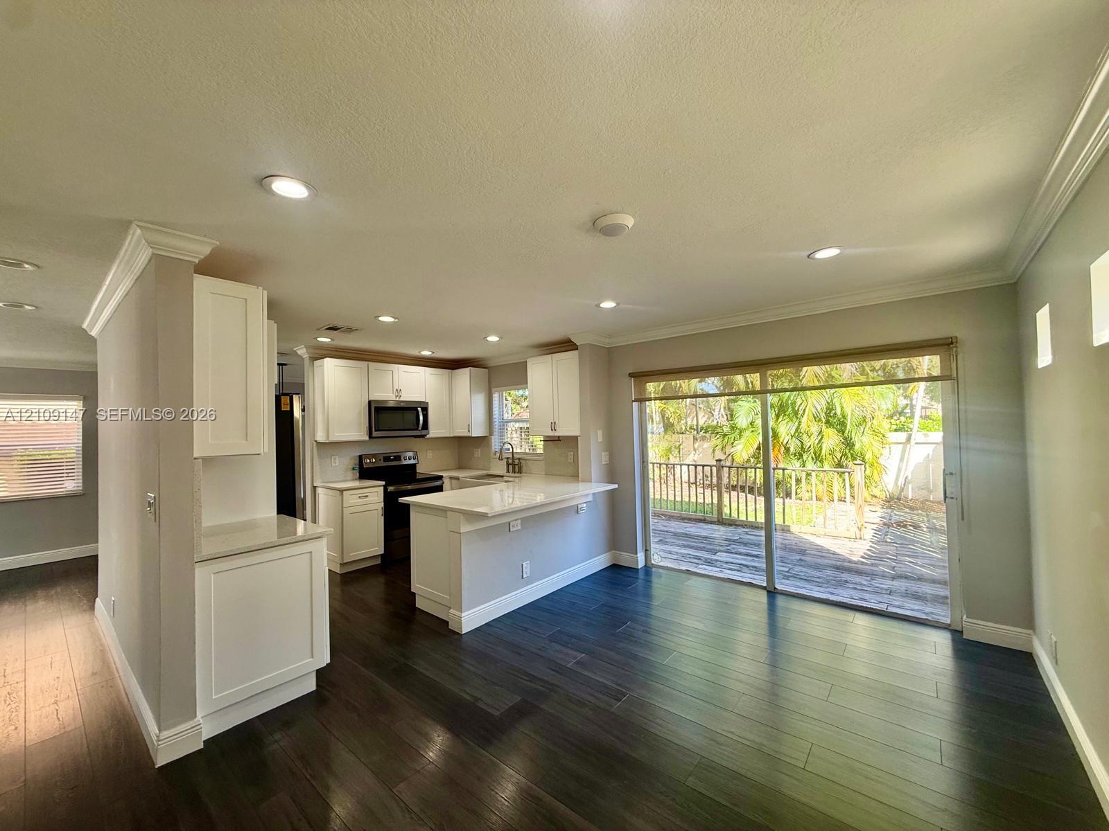 Kitchen featuring white cabinetry, solid-surface countertops, a breakfast bar, recessed lighting, and dark wood-finish flooring