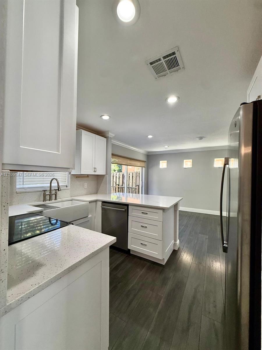 Kitchen featuring white shaker-style cabinetry, solid-surface countertops, a farmhouse-style sink, stainless steel appliances, and wood-finish flooring