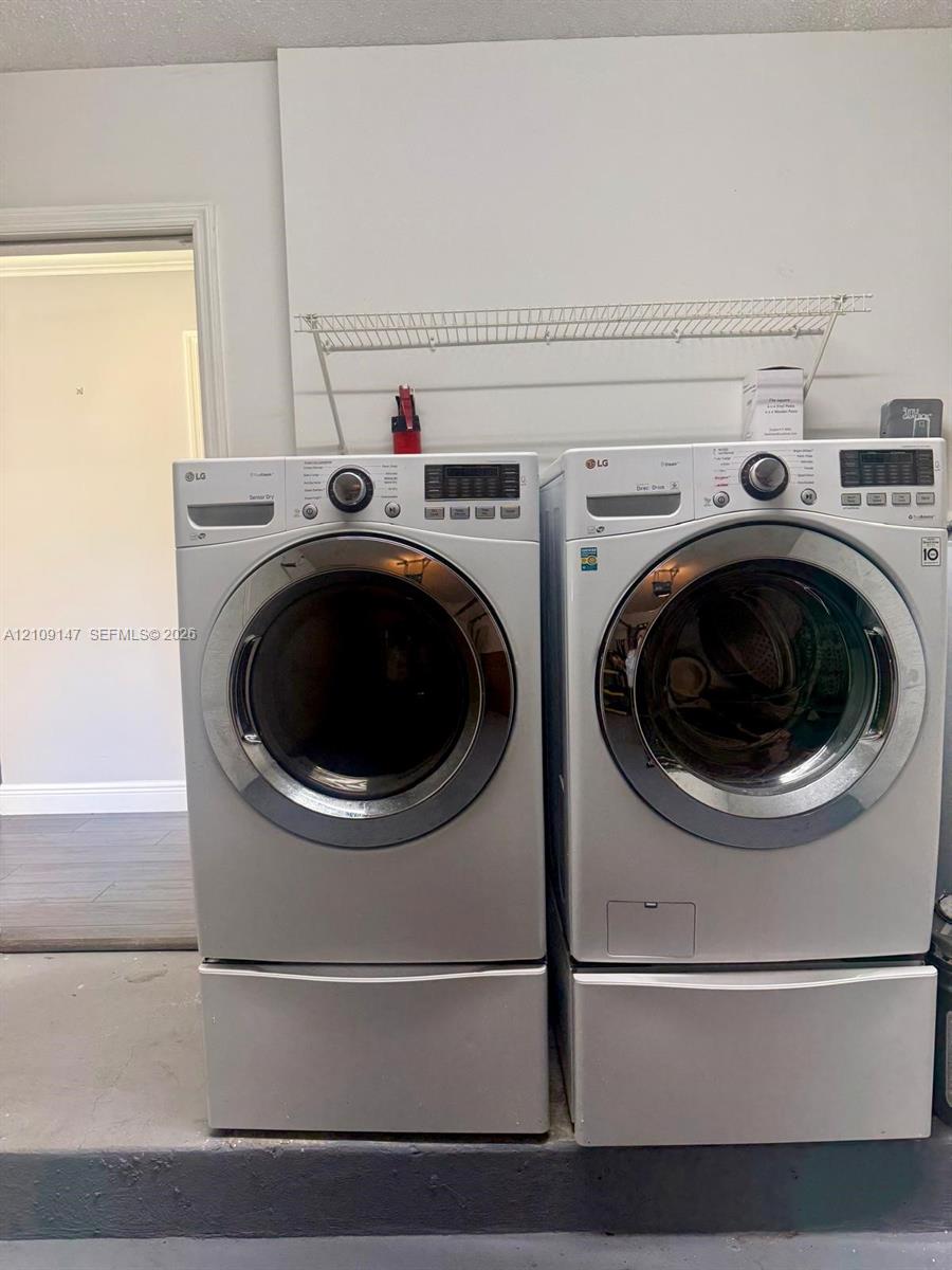 Laundry area featuring two front-loading machines with integrated drawer pedestals and a wall-mounted wire storage shelf