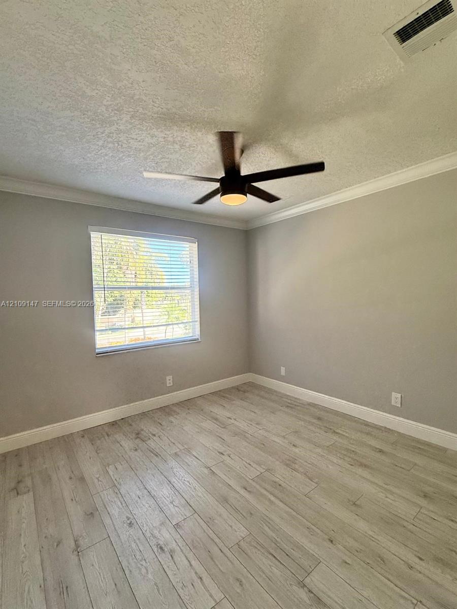 Neutral interior featuring wood-finish flooring, crown molding, and a central ceiling fan with integrated lighting Neutral interior featuring wood-finish flooring, crown molding, and a central ceiling fan with integrated lighting