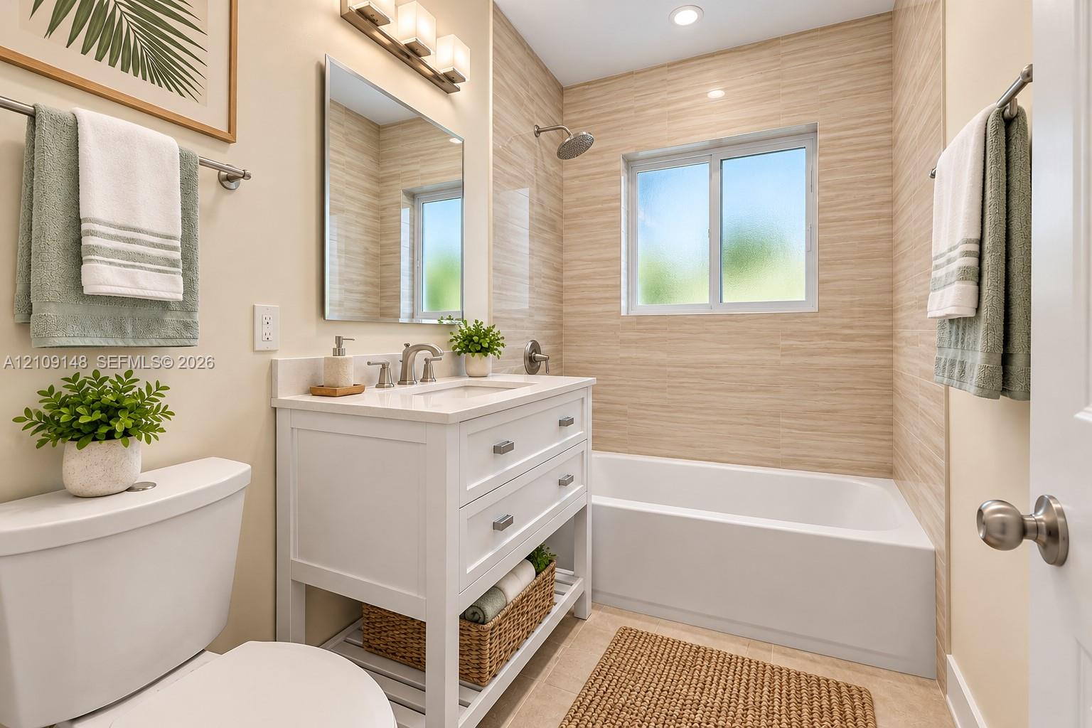 White vanity with dual soft-close drawers and an open lower shelf, rectangular sink with polished chrome hardware, framed mirror with three-light vanity bar fixture, and floor-to-ceiling textured tile surrounding a built-in soaking tub