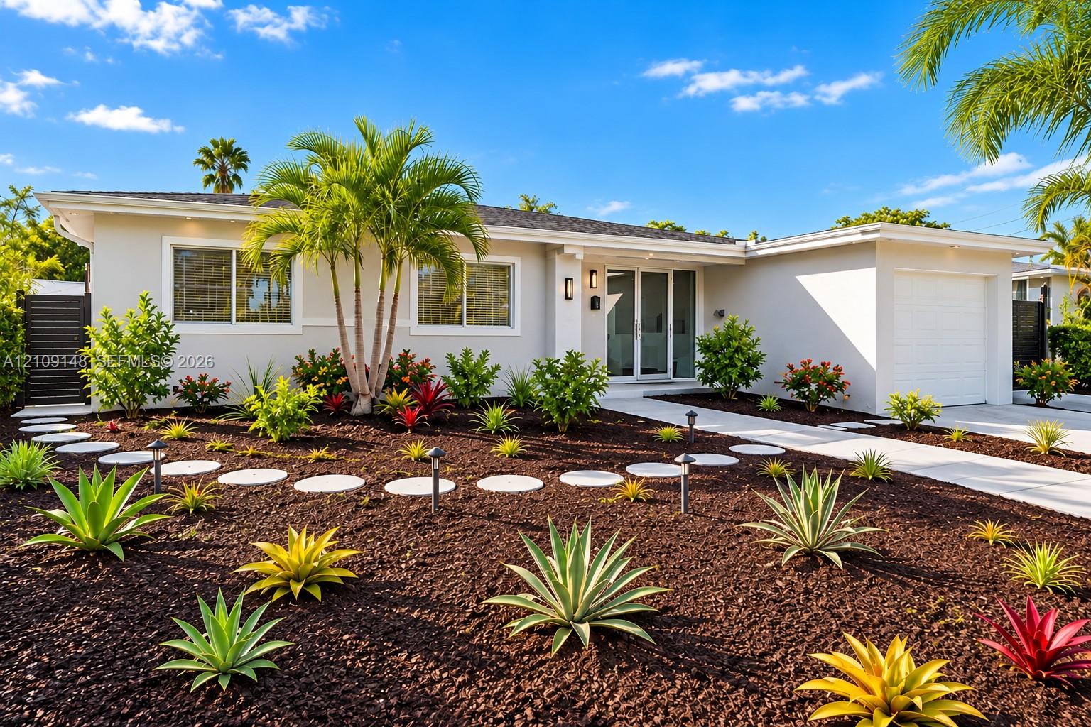 Single-story exterior featuring light-toned smooth stucco, a concrete paver walkway, professional xeric landscaping, mature palm trees, and an attached garage
