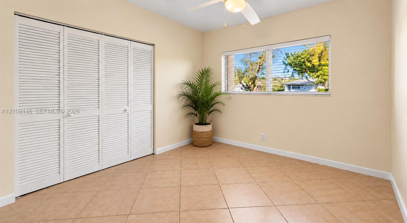 Room featuring neutral-toned tile flooring, louvered bi-fold closet doors, horizontal windows, and a ceiling-mounted light fixture