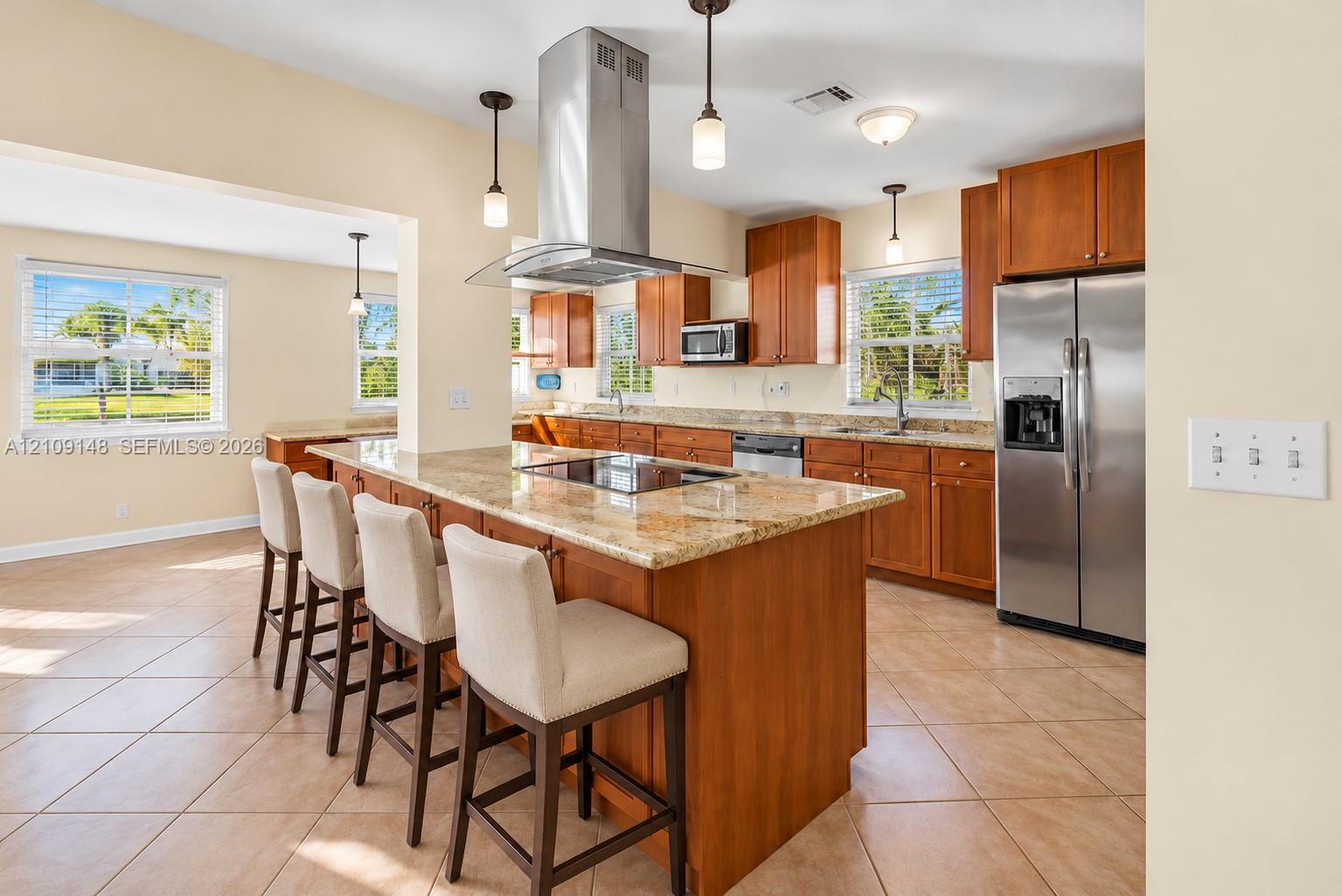 Kitchen featuring a center island with an integrated cooktop, stone-surface countertops, stainless steel appliances, custom wood cabinetry, and pendant lighting