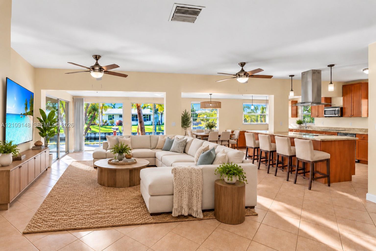 Open-concept living space featuring ceramic tile flooring, kitchen island with breakfast bar, stainless steel range hood, built-in cabinetry, and sliding glass doors
