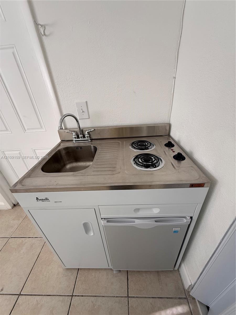 Compact kitchenette unit featuring a stainless steel integrated sink and dual-burner electric cooktop, white cabinetry, and a built-in under-counter refrigerator