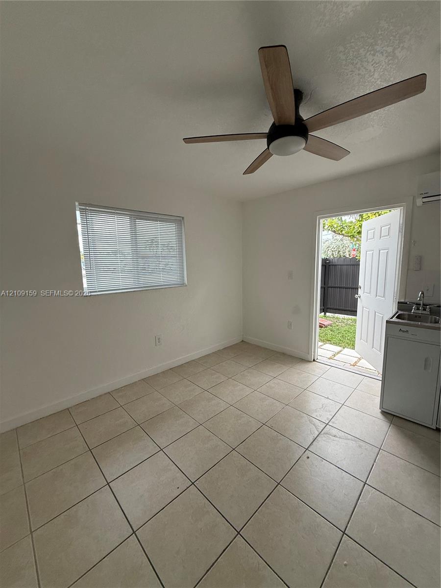 Tile flooring, ceiling fan with integrated lighting, horizontal sliding window with blinds, wall-mounted air conditioning unit, and built-in kitchenette area with sink Tile flooring, ceiling fan with integrated lighting, horizontal sliding window with blinds, wall-mounted air conditioning unit, and built-in kitchenette area with sink