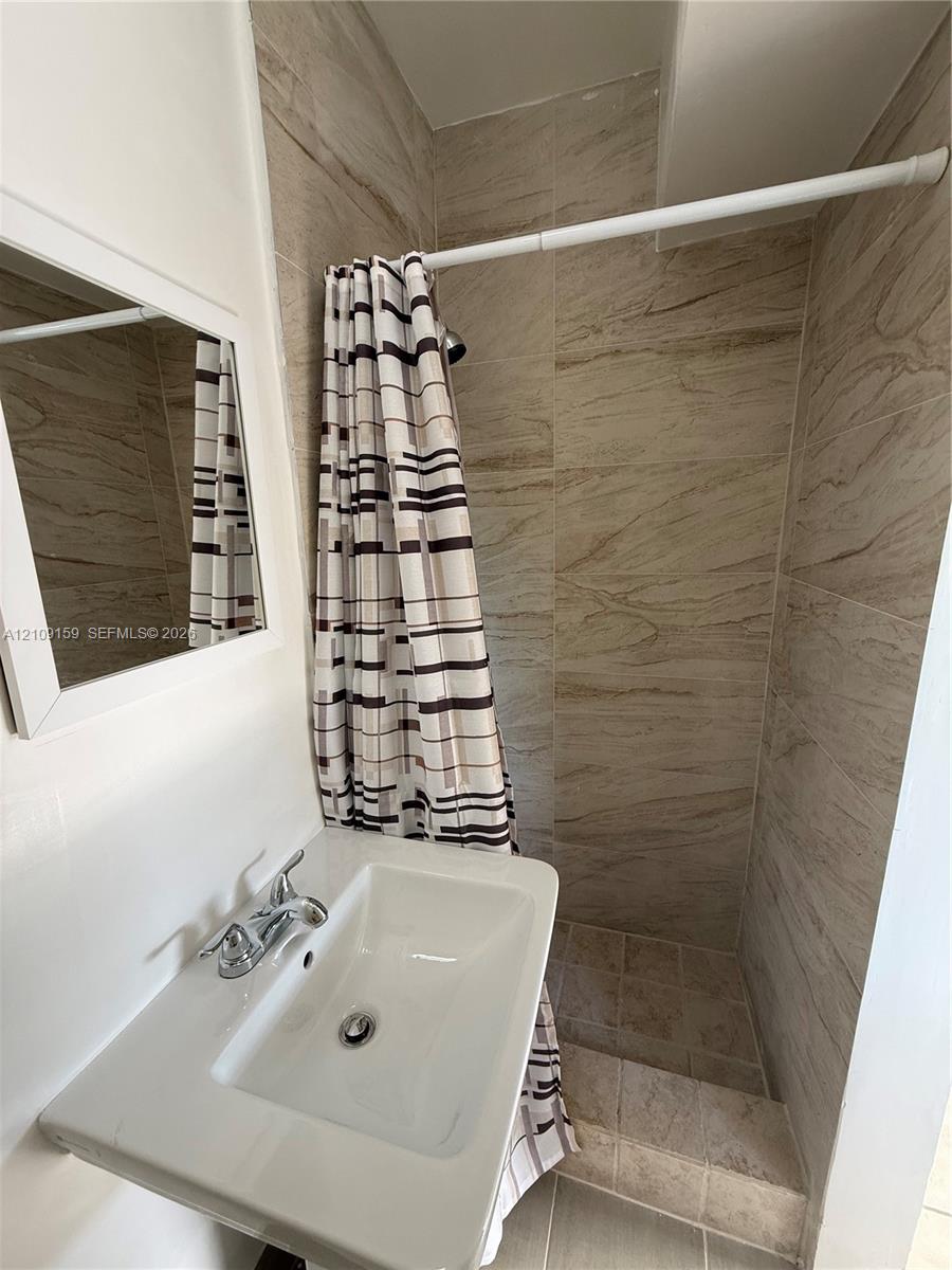Wall-mounted white basin sink featuring chrome dual-handle hardware, framed vanity mirror, and walk-in shower enclosure finished with neutral-toned stone-style tile