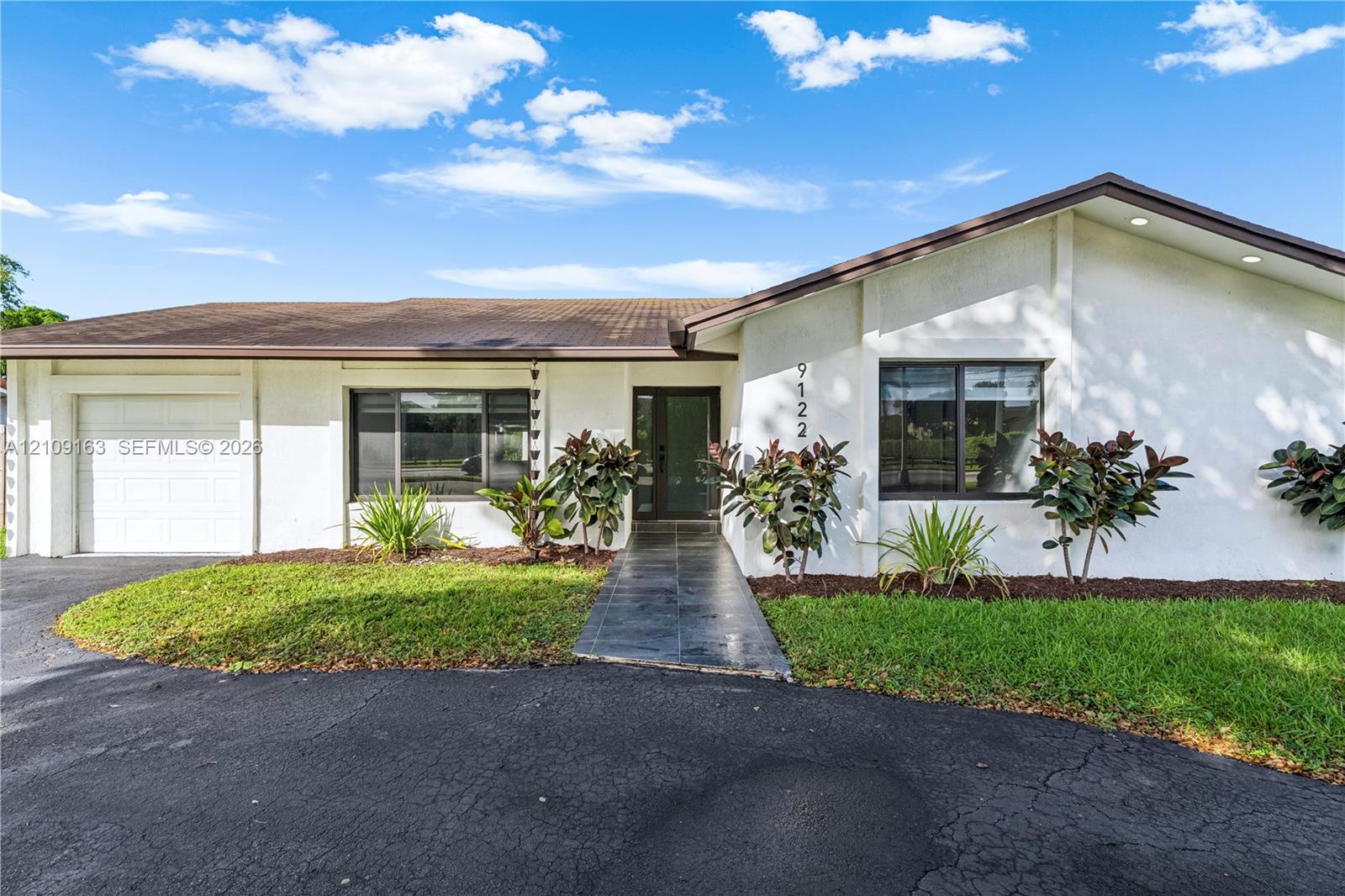 Single-story exterior featuring white stucco siding, a tiled roof, a paved walkway, a multi-pane glass entry door, and an attached garage Single-story exterior featuring white stucco siding, a tiled roof, a paved walkway, a multi-pane glass entry door, and an attached garage