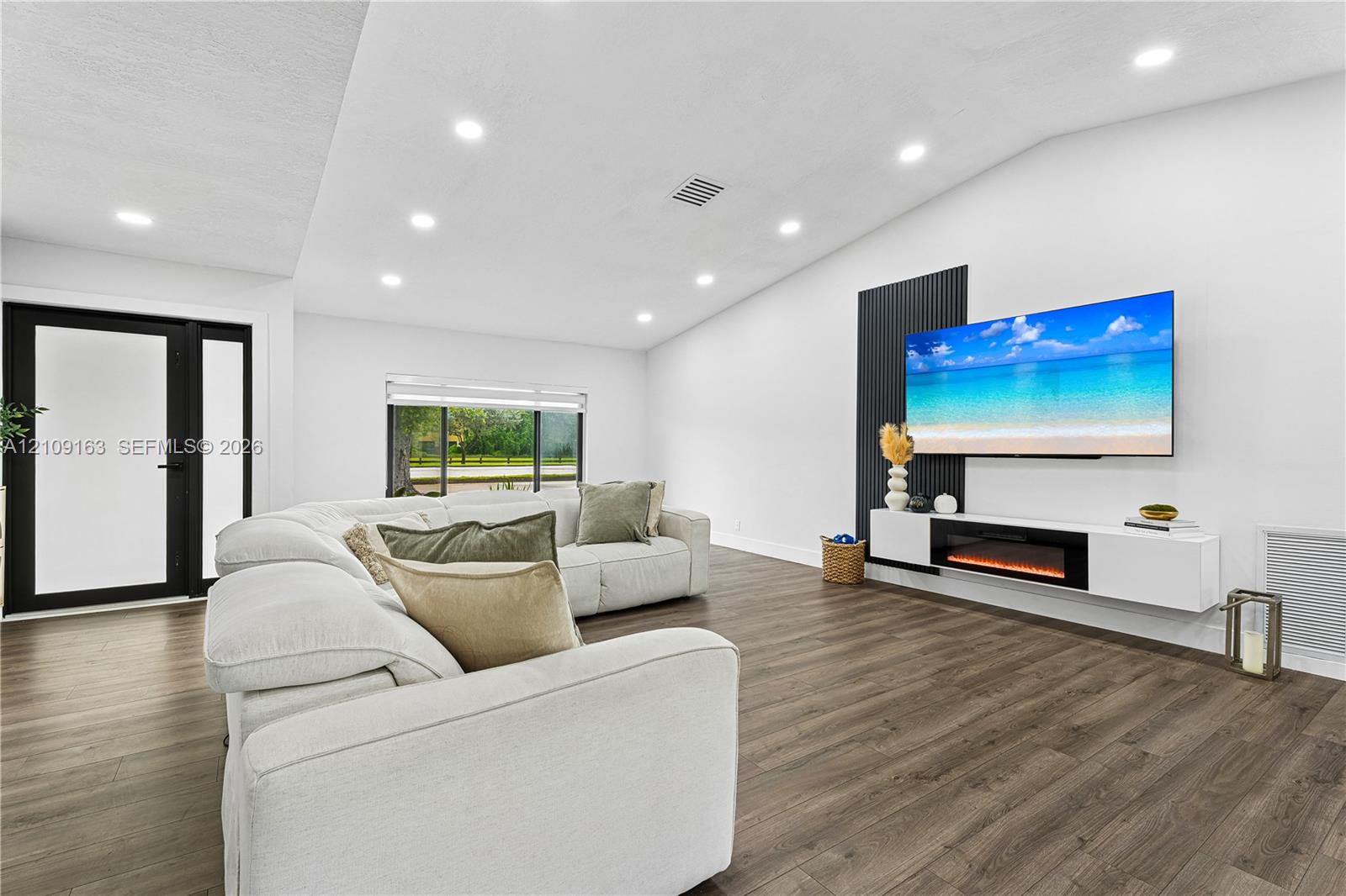 Vaulted ceilings with recessed lighting, wood-finish flooring, a black vertical-slatted accent wall, and a wall-mounted floating media console with an integrated electric fireplace