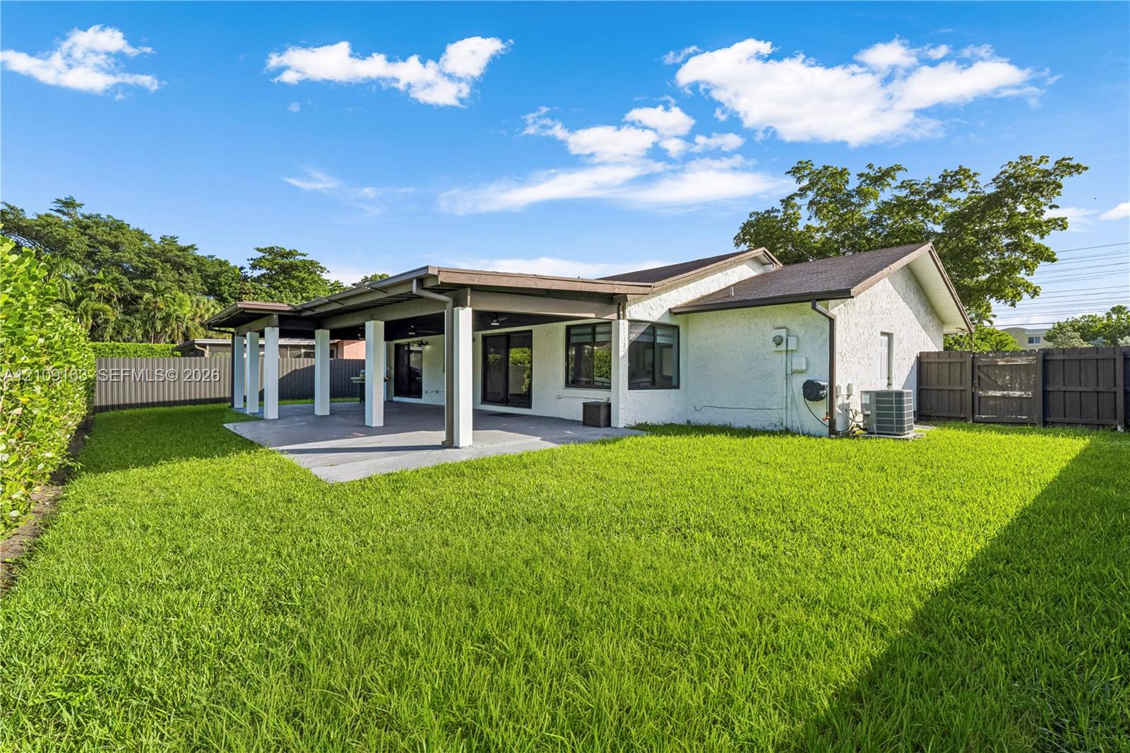 Expansive backyard featuring a manicured lawn, a covered concrete patio with structural columns, and enclosed perimeter fencing