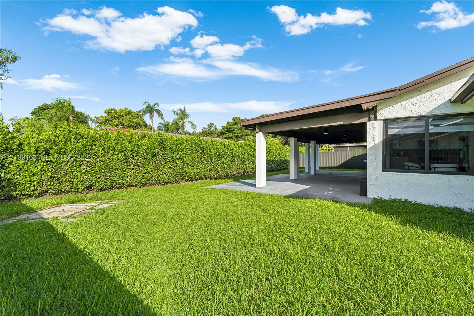 Rear yard featuring a manicured lawn, paved covered patio, stucco exterior finish, and dense perimeter hedging
