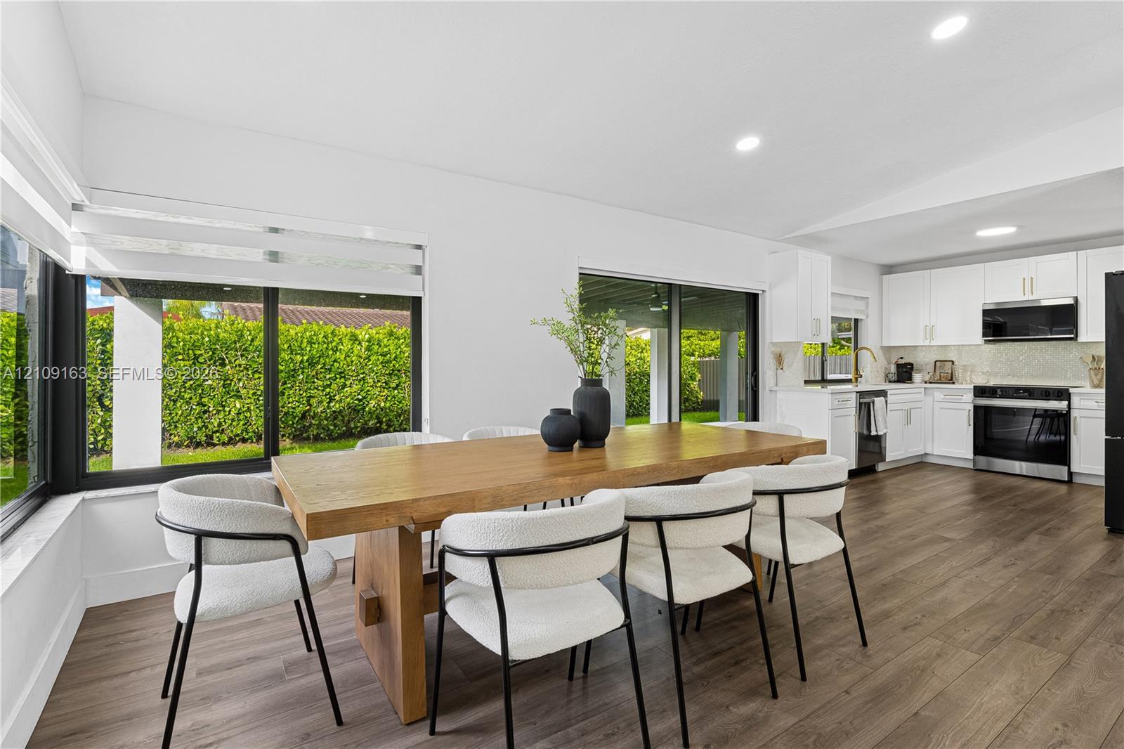 Open-concept kitchen and dining area featuring wood-finish flooring, recessed lighting, white shaker-style cabinetry, and large sliding glass doors