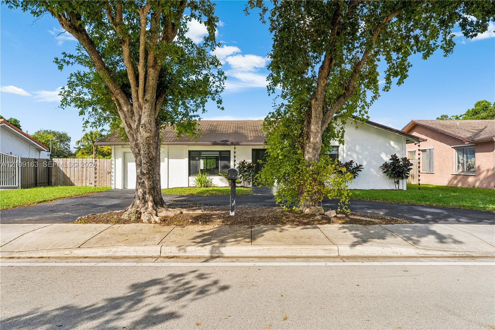 Single-story exterior featuring white stucco siding, a concrete tile roof, a paved driveway, and mature landscaping