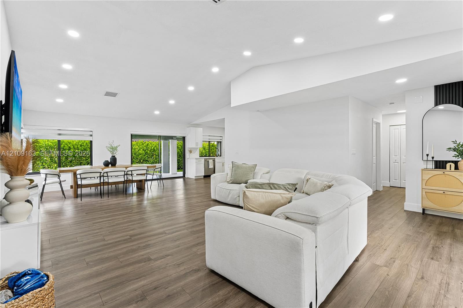 Open-concept living space featuring high vaulted ceilings, recessed lighting, wood-finish flooring, and large sliding glass doors