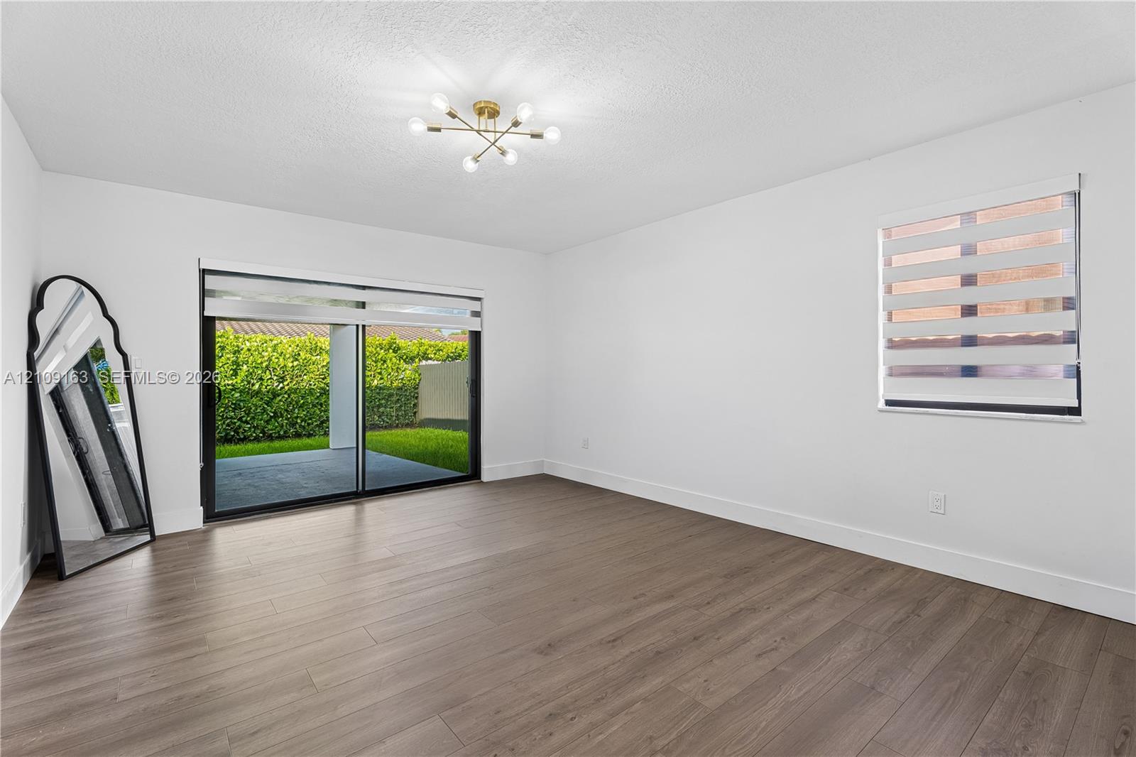 Spacious room featuring wood-finish flooring, a modern sputnik-style ceiling light fixture, sliding glass doors, and dual-layered window shades
