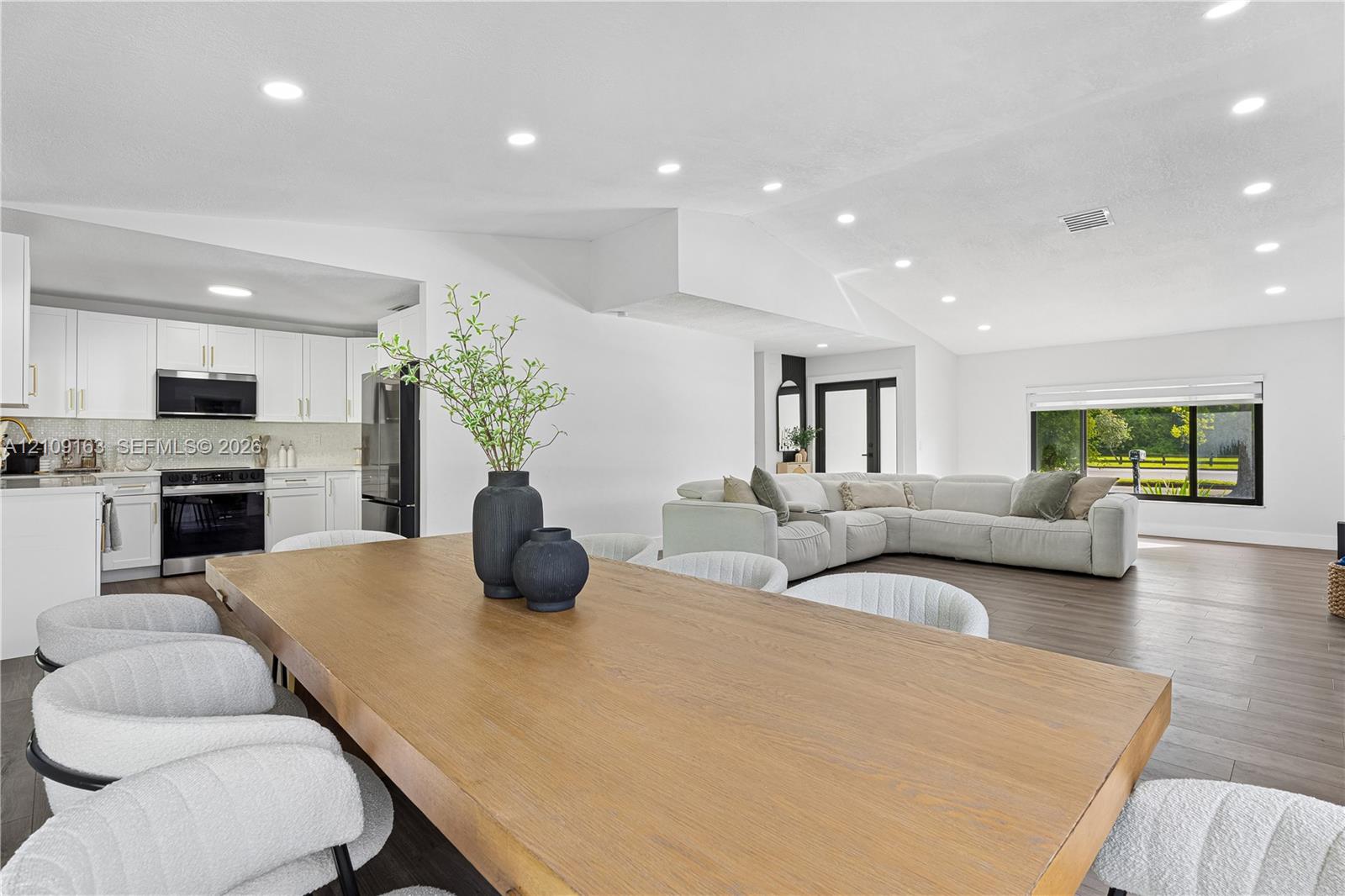 Open-concept interior featuring vaulted ceilings, recessed lighting, wood-finish flooring, and crisp white cabinetry