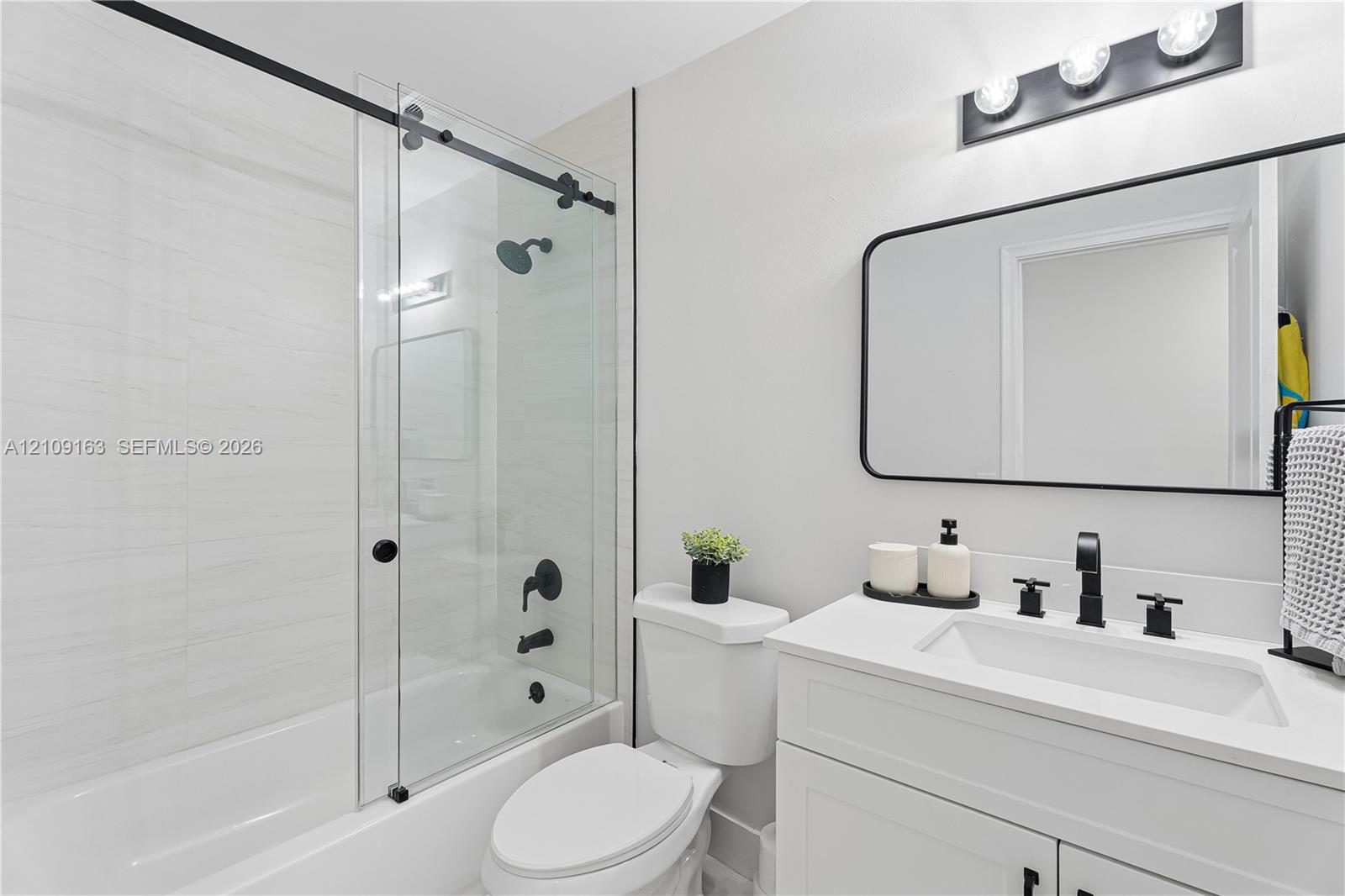 Bathroom featuring a vanity with a white countertop and rectangular undermount sink, a glass sliding shower door with matte black hardware, horizontal wall tile, and a rectangular mirror with a black frame