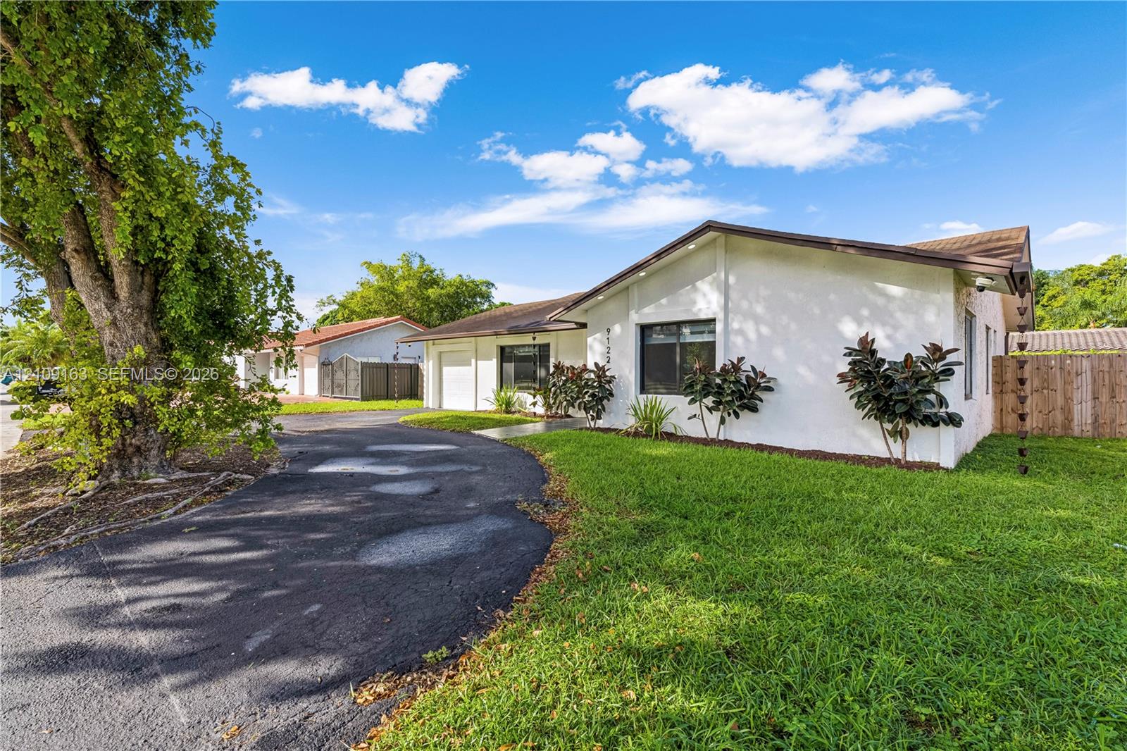 Single-story residence featuring a white stucco exterior, asphalt driveway, manicured lawn, and wood-panel fencing