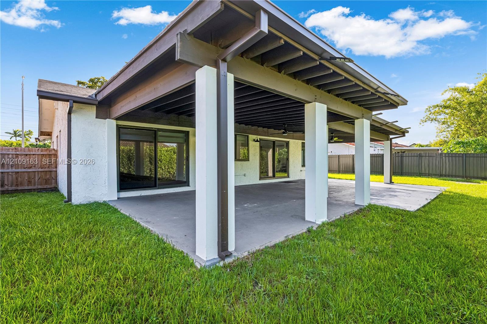 Covered outdoor patio featuring exposed wood-beam ceiling, concrete flooring, square structural support columns, and sliding glass door access