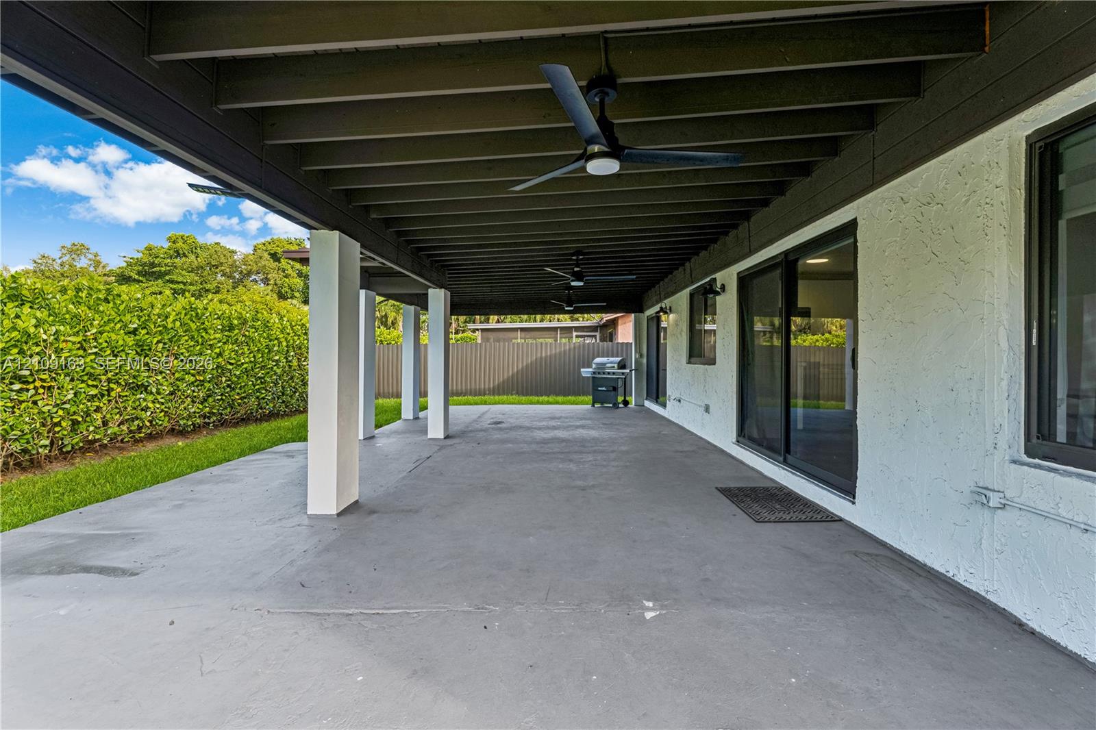Covered outdoor patio featuring a painted concrete floor, exposed beam ceiling, multiple mounted ceiling fans, and sliding glass door access