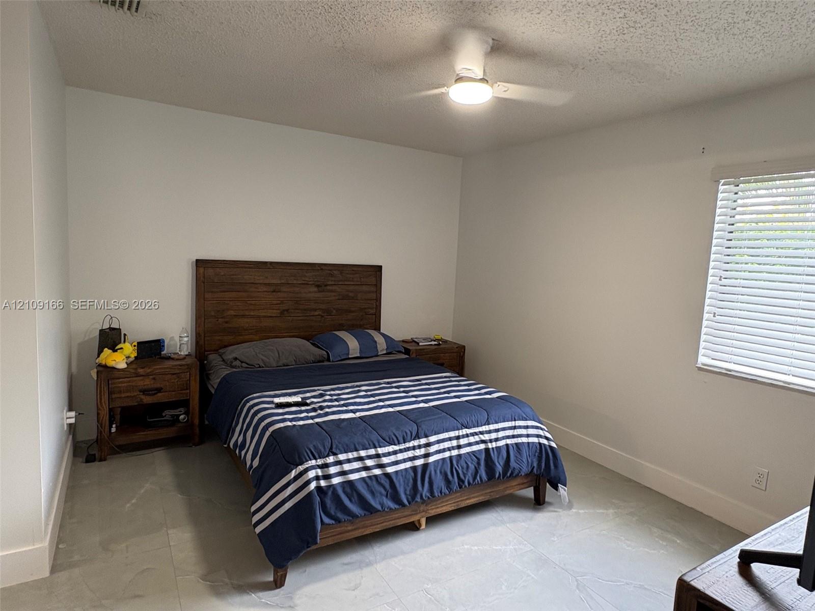 Neutral-toned tile flooring, white wall finish, white horizontal window blinds, and a white ceiling fan with an integrated light fixture