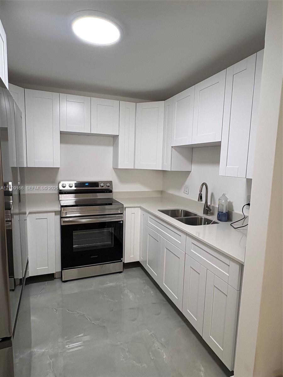 Kitchen featuring white shaker-style cabinetry, solid-surface countertops, dual-basin stainless steel sink with high-arch faucet, stainless steel electric range, and polished finish flooring