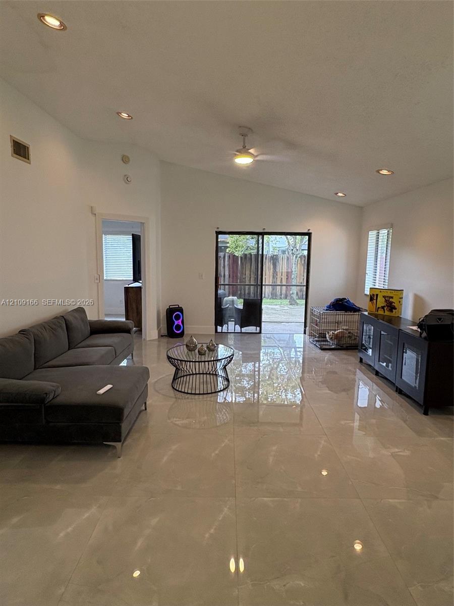 Vaulted ceiling with recessed lighting, large-format tile flooring, and sliding glass doors leading to an outdoor patio