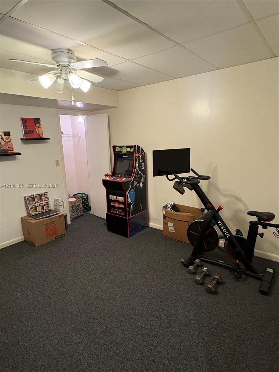 Neutral-toned interior space featuring dark wall-to-wall carpeting, a drop ceiling, a ceiling-mounted light fixture with four glass shades, and an enclosed storage closet