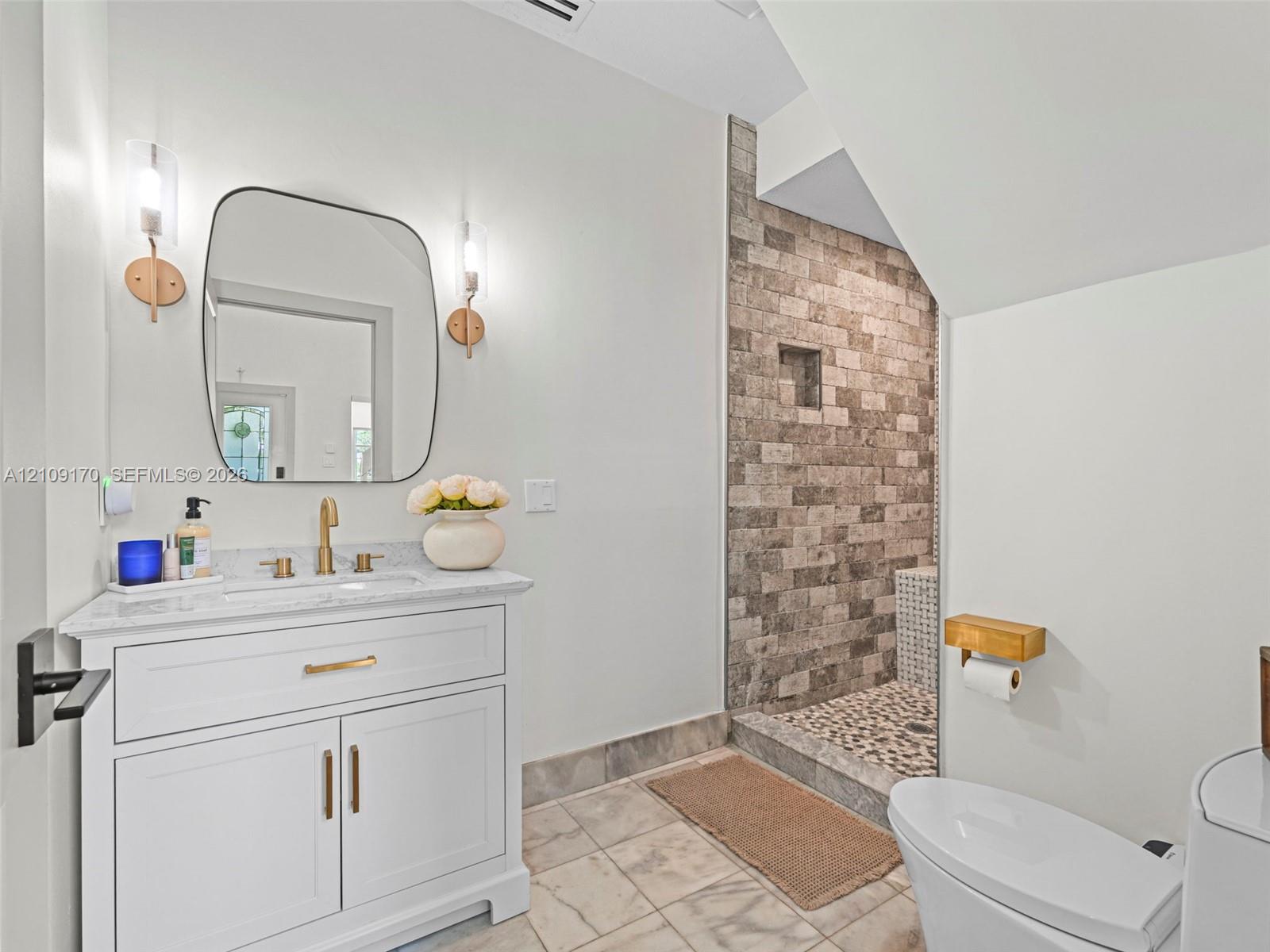 White vanity with stone countertop, undermount sink, and brass finish faucet