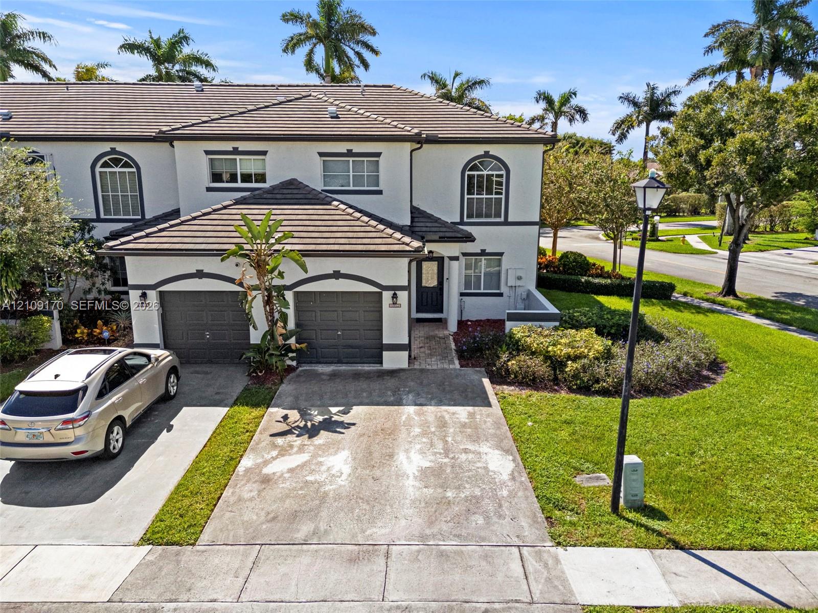 Two-story exterior featuring light-toned stucco walls, arched window detailing, a concrete tile roof, and a two-car garage