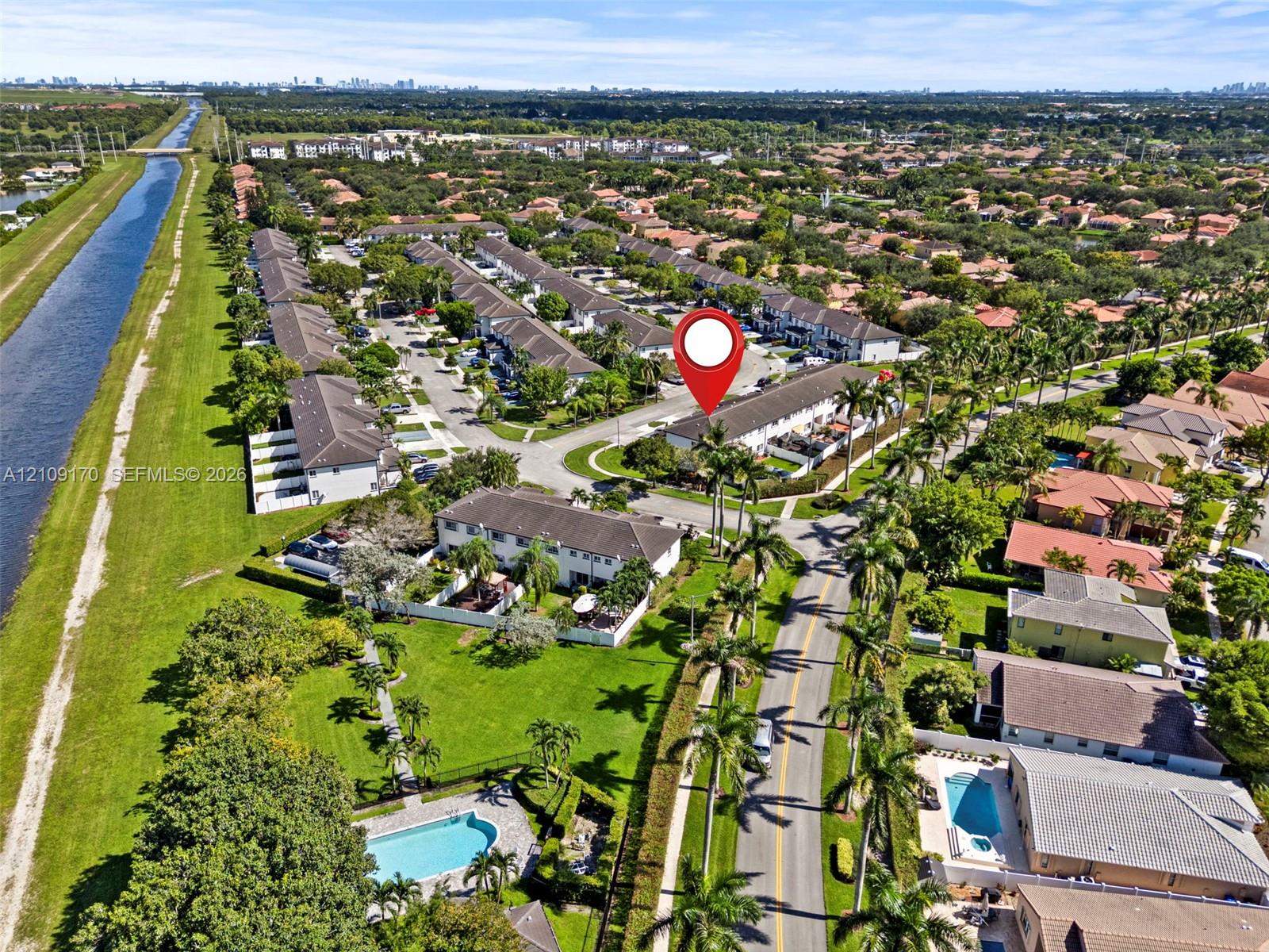 Aerial perspective of a multi-unit residential community featuring manicured landscaping, palm trees, and an open-air swimming pool