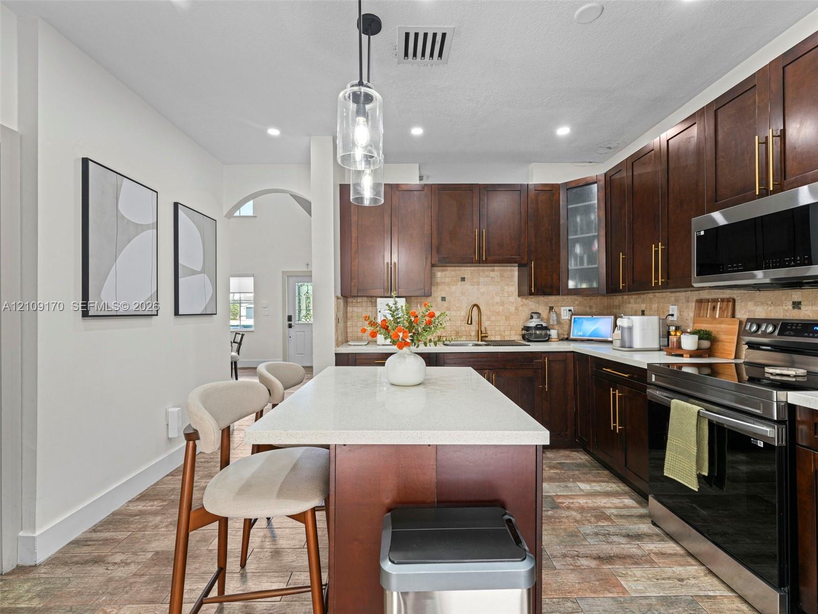 Kitchen featuring dark wood cabinetry, quartz countertops, a central island, stainless steel appliances, and tile backsplash