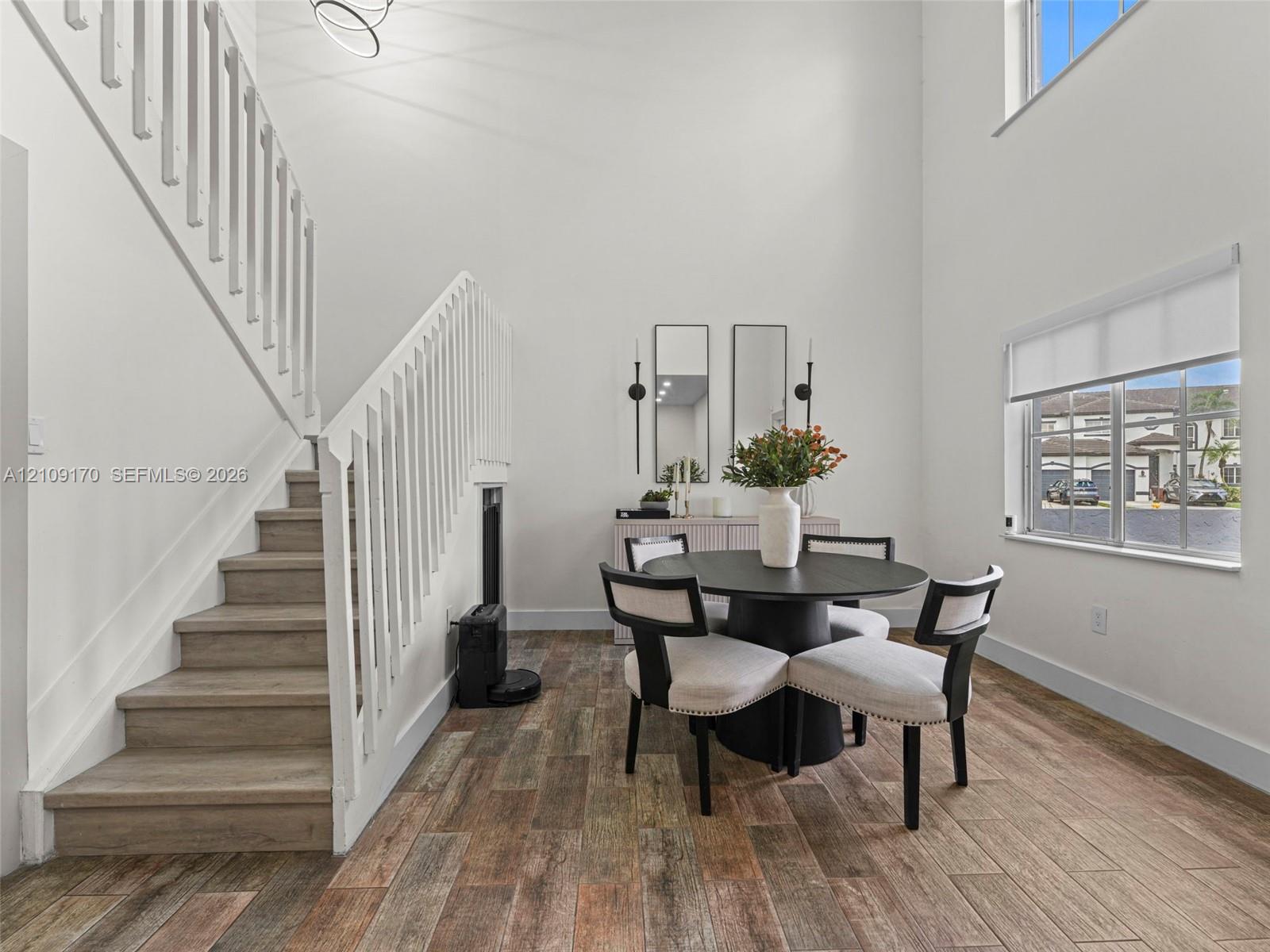 Double-height ceiling, staircase with white wood balusters, wood-finish flooring, and multi-pane windows Double-height ceiling, staircase with white wood balusters, wood-finish flooring, and multi-pane windows