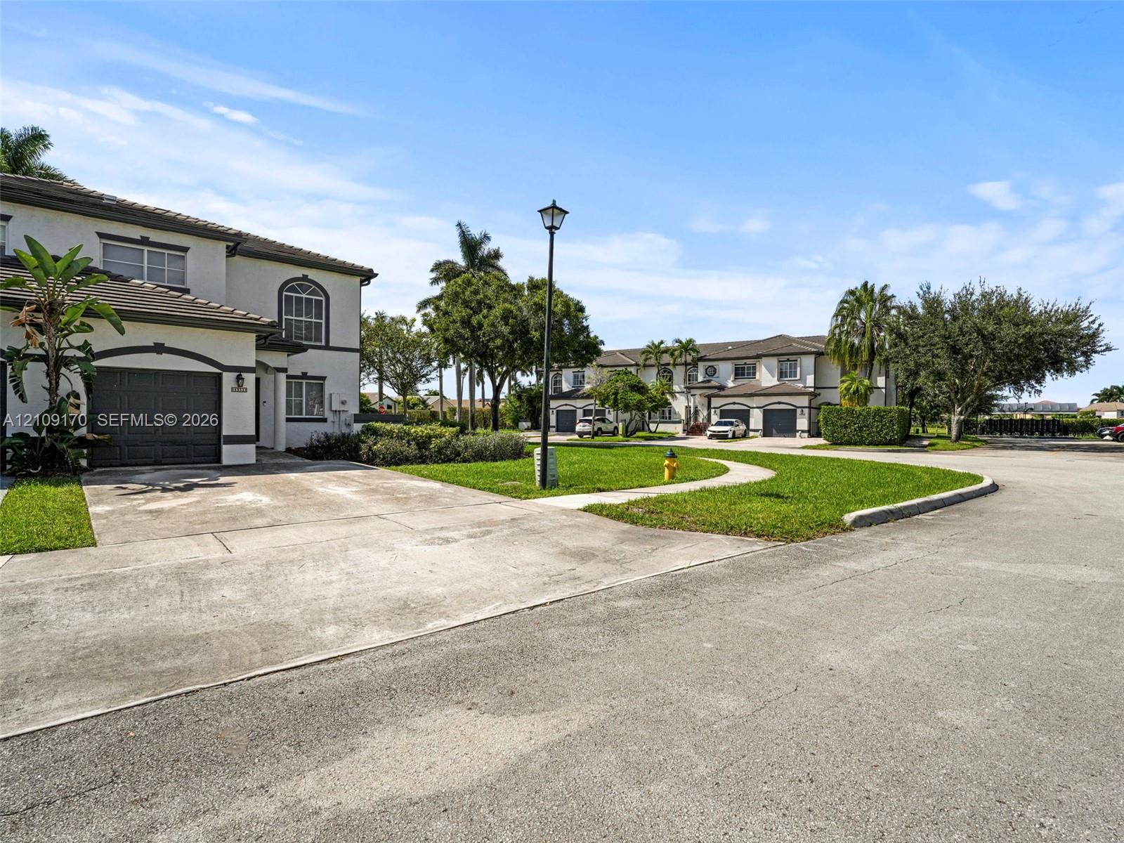 Stucco exterior featuring a dark-toned tile roof, arched window detailing, and an attached single-car garage with a concrete driveway, set within a landscaped common area with paved walkways