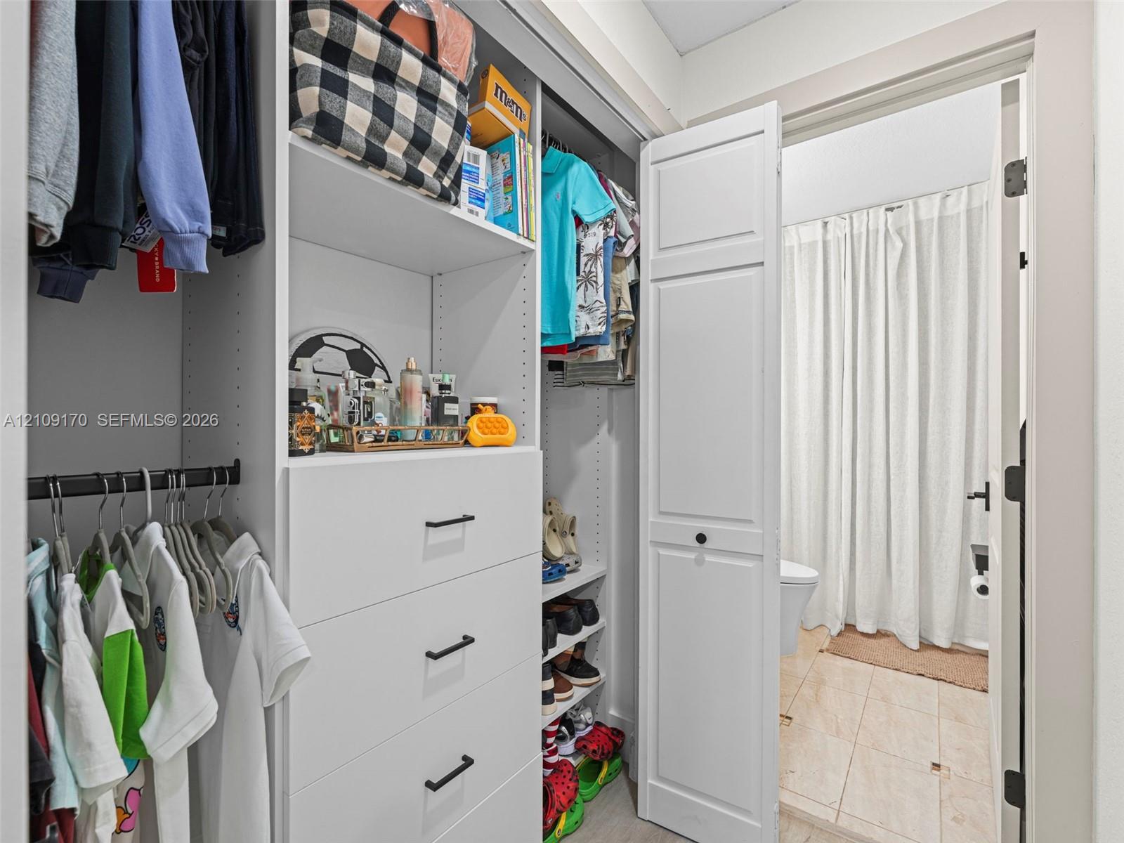 Custom built-in closet organization system featuring white cabinetry, adjustable shelving, integrated storage drawers with matte black hardware, and hanging rods