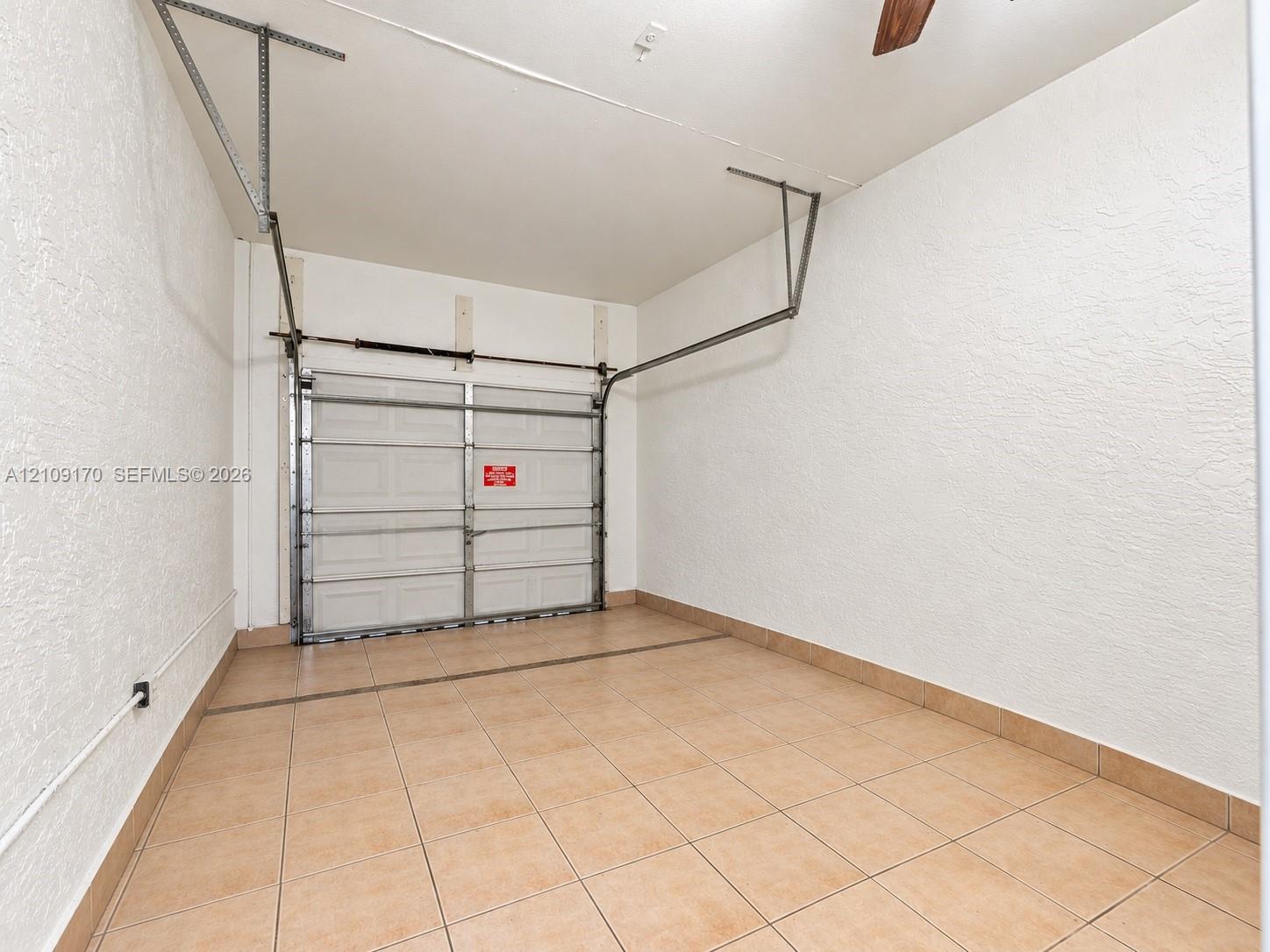 Enclosed garage featuring textured wall finishes, ceramic tile flooring, and a metal sectional overhead door