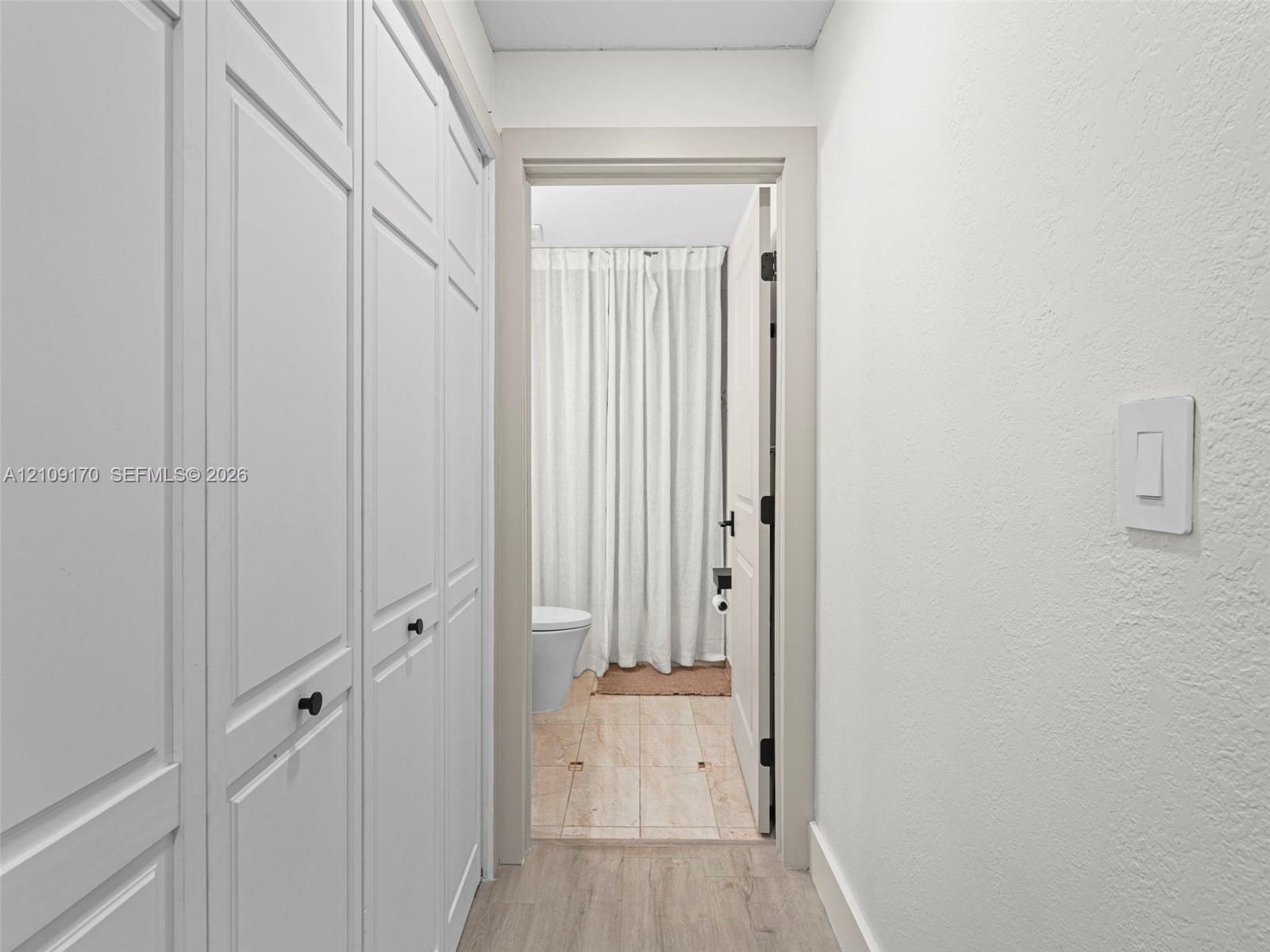 Hallway featuring floor-to-ceiling white paneled storage cabinetry with matte black hardware and wood-finish flooring